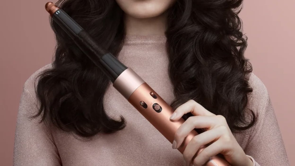 close up of woman using Dyson Airwrap i.d. with pink background