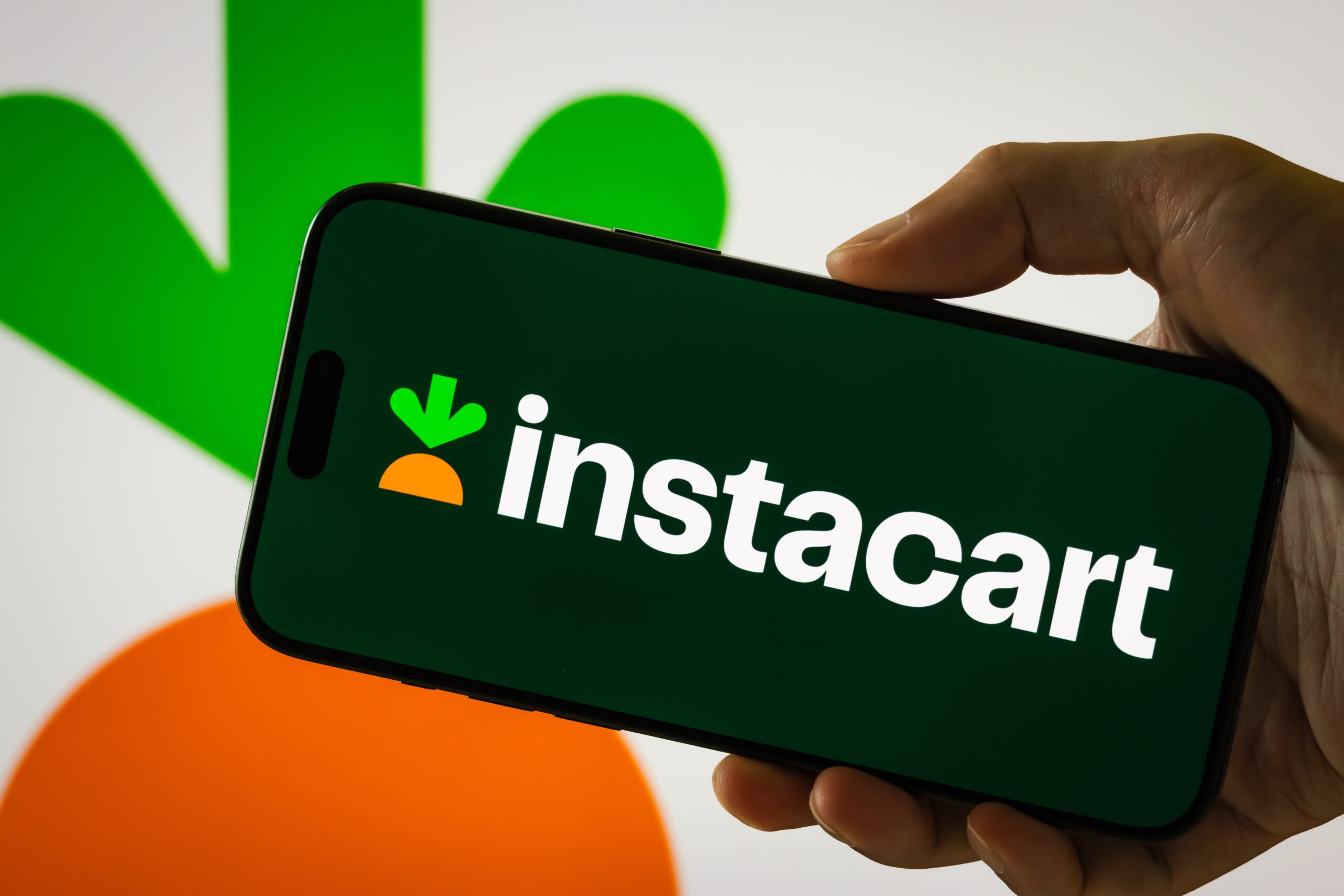 person holds a smartphone displaying Instacart logo