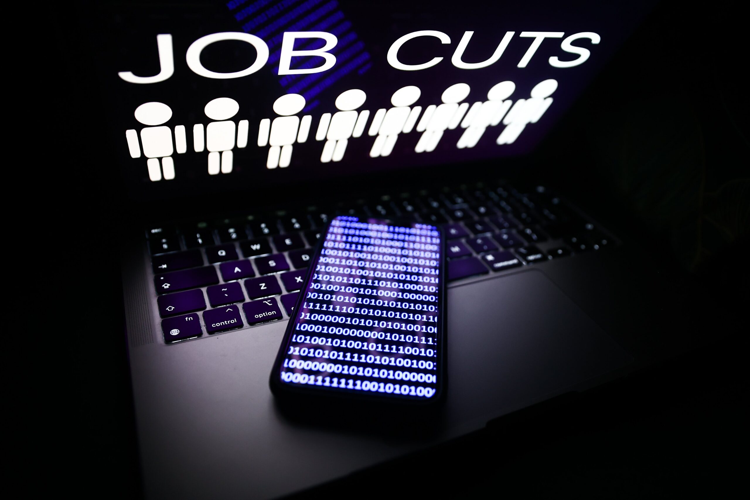 'Job cuts' sign and stick figures image displayed on a laptop screen and a binary code displayed on a phone screen are seen in this illustration photo taken in Krakow, Poland on January 25, 2023.