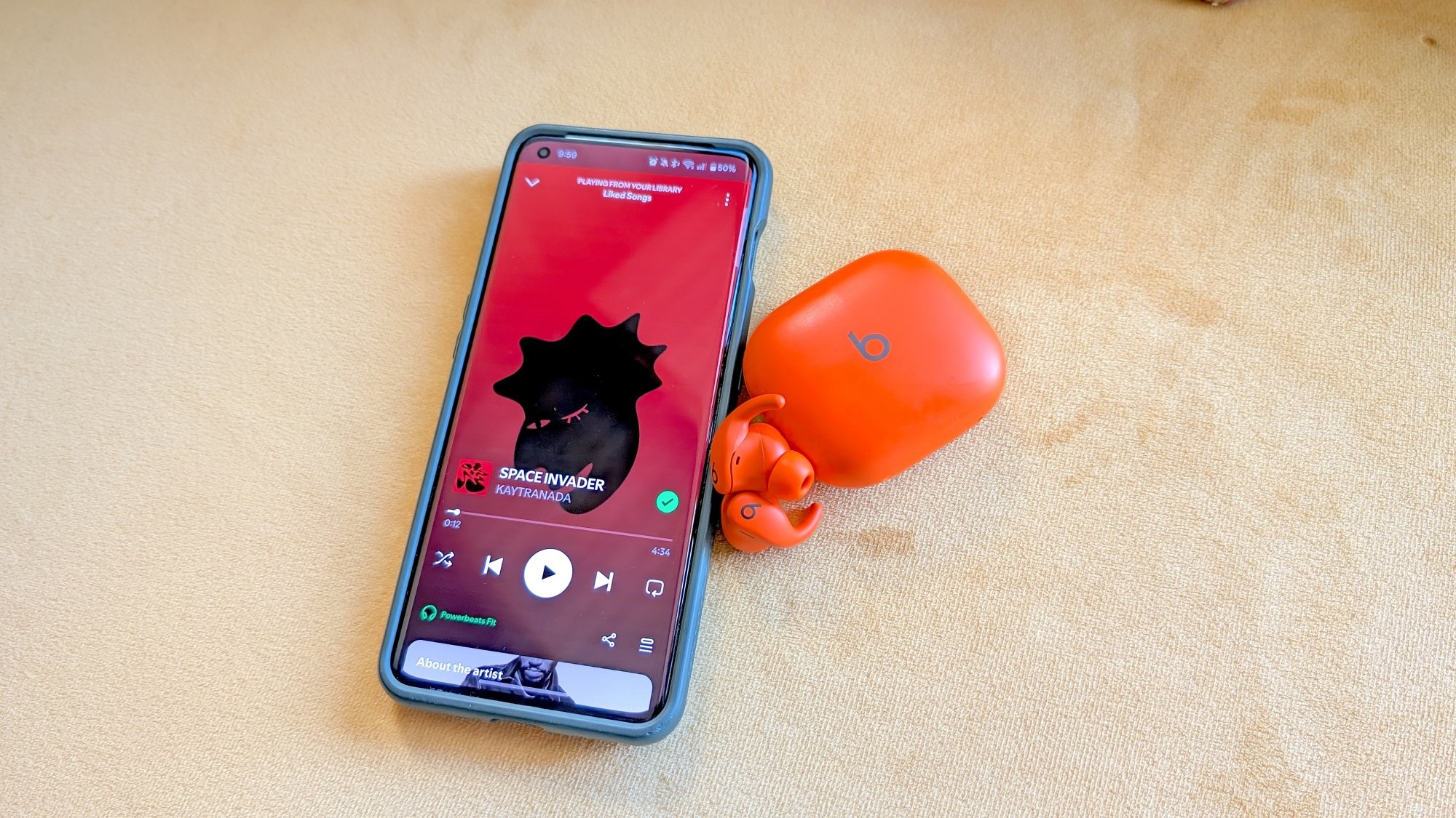 orange beats powerbeats fit earbuds next to phone with spotify open