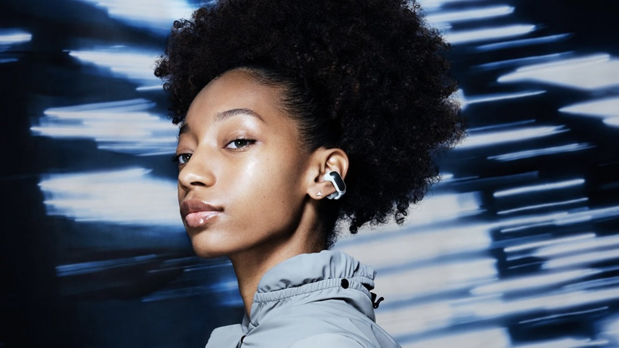 person on blue background wearing white and silver bose ultra open earbud