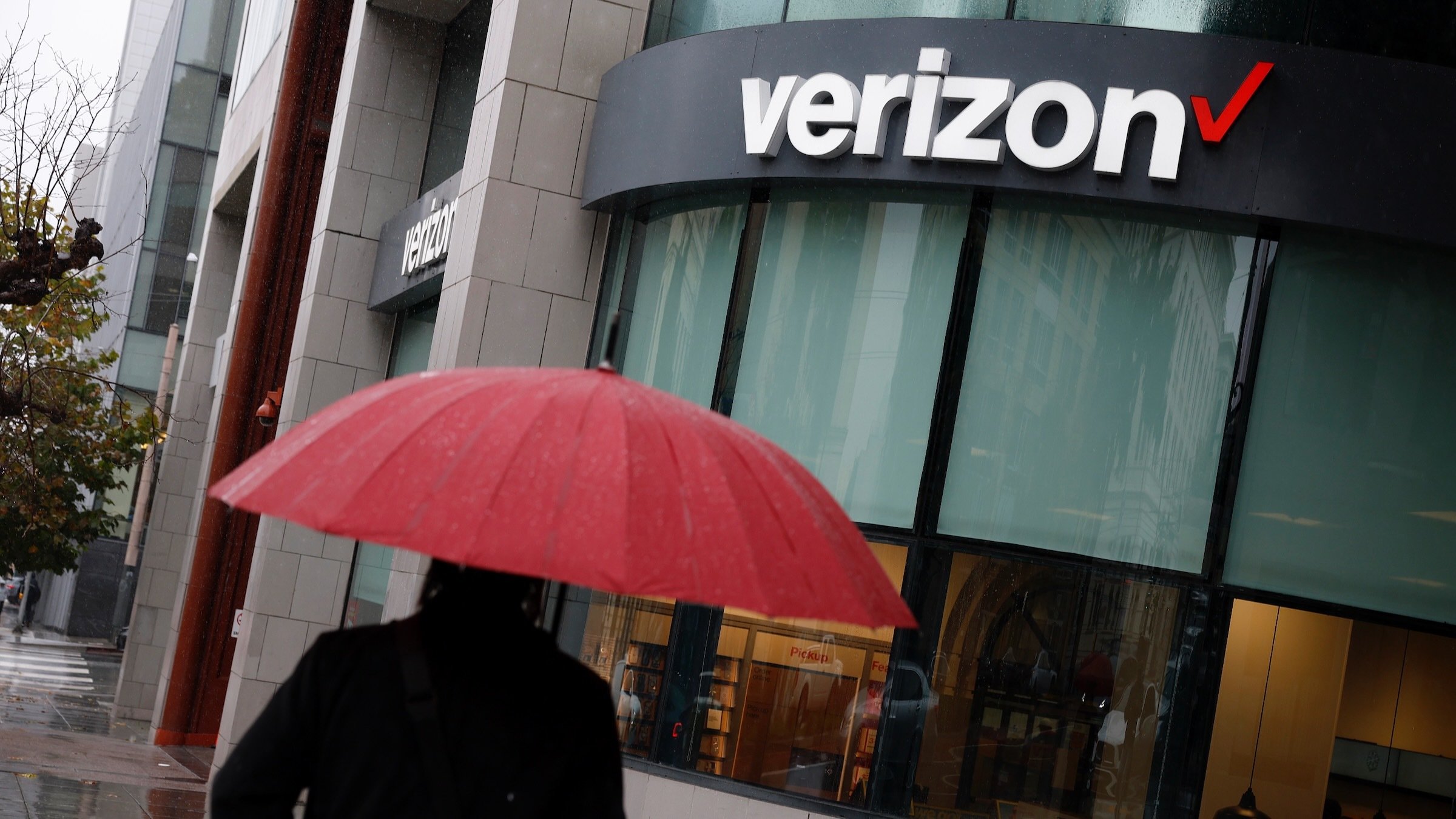 a person with an umbrella walks past a verizon store on a rainy day