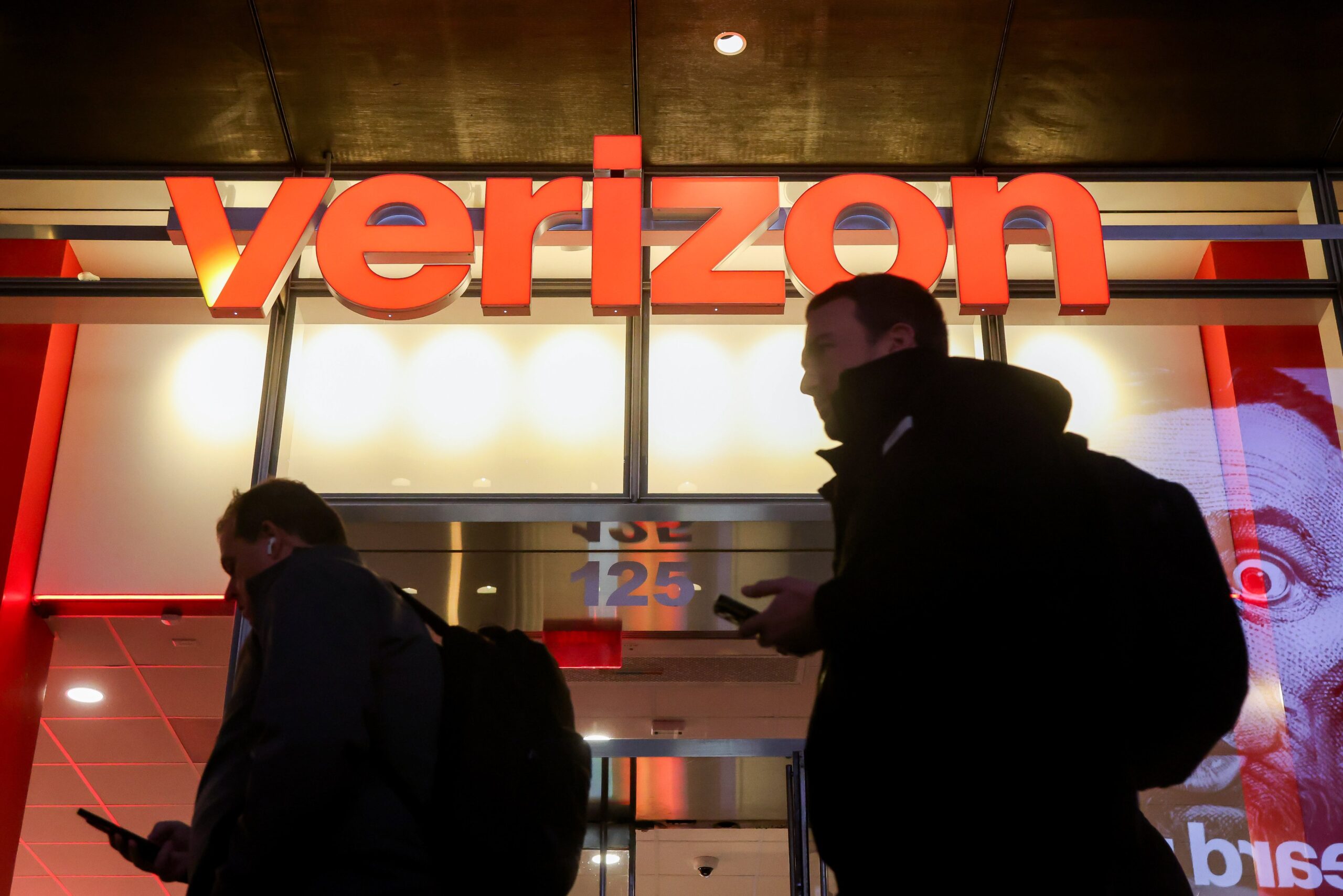 People walk by a Verizon storefront in the evening.