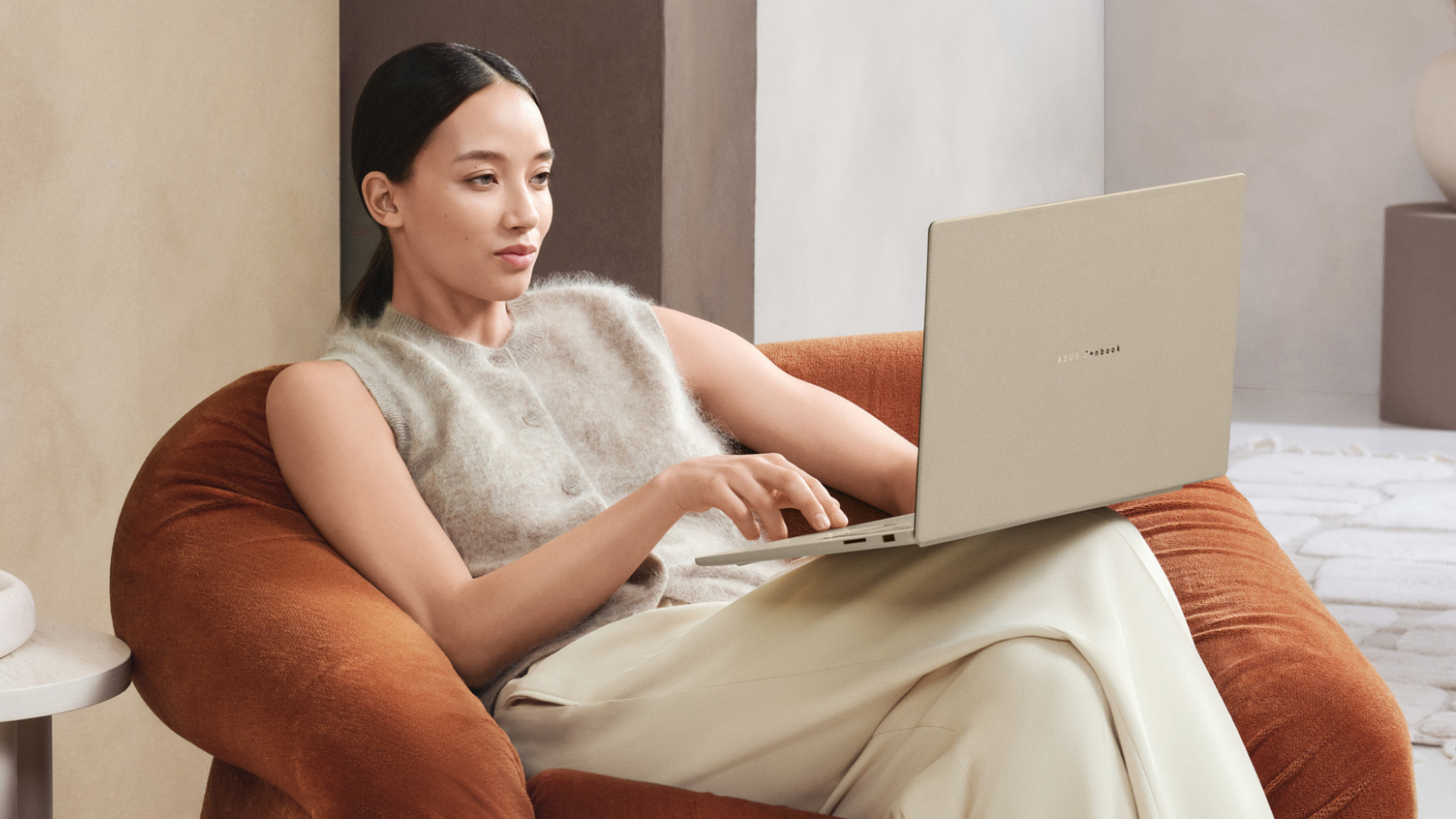 a woman sitting on a chair while typing on the asus zenbook a16