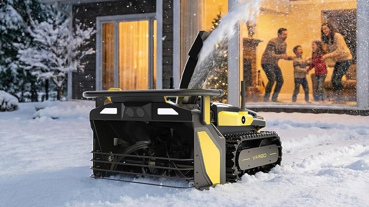 the yarbo robot snow blower removes snow in the dark while a home with a big window sits behind the robot. Inside, a family is looking outside while smiling.