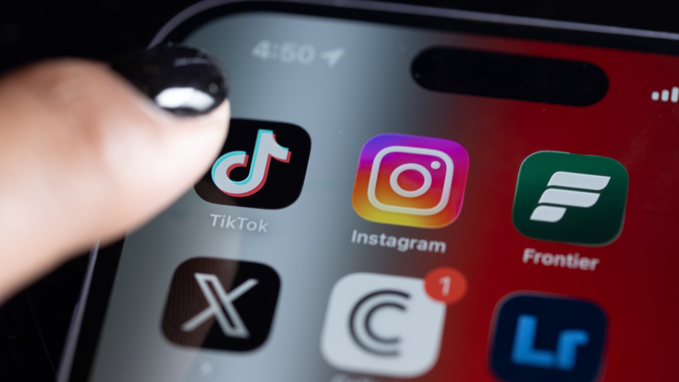 A thumb hovers over the TikTok app on an iPhone screen.