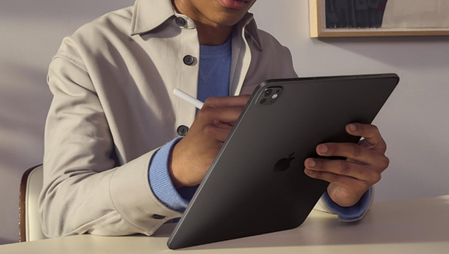 a person holds the m5 ipad pro 11-inch while sitting a desk and writing with the apple pencil