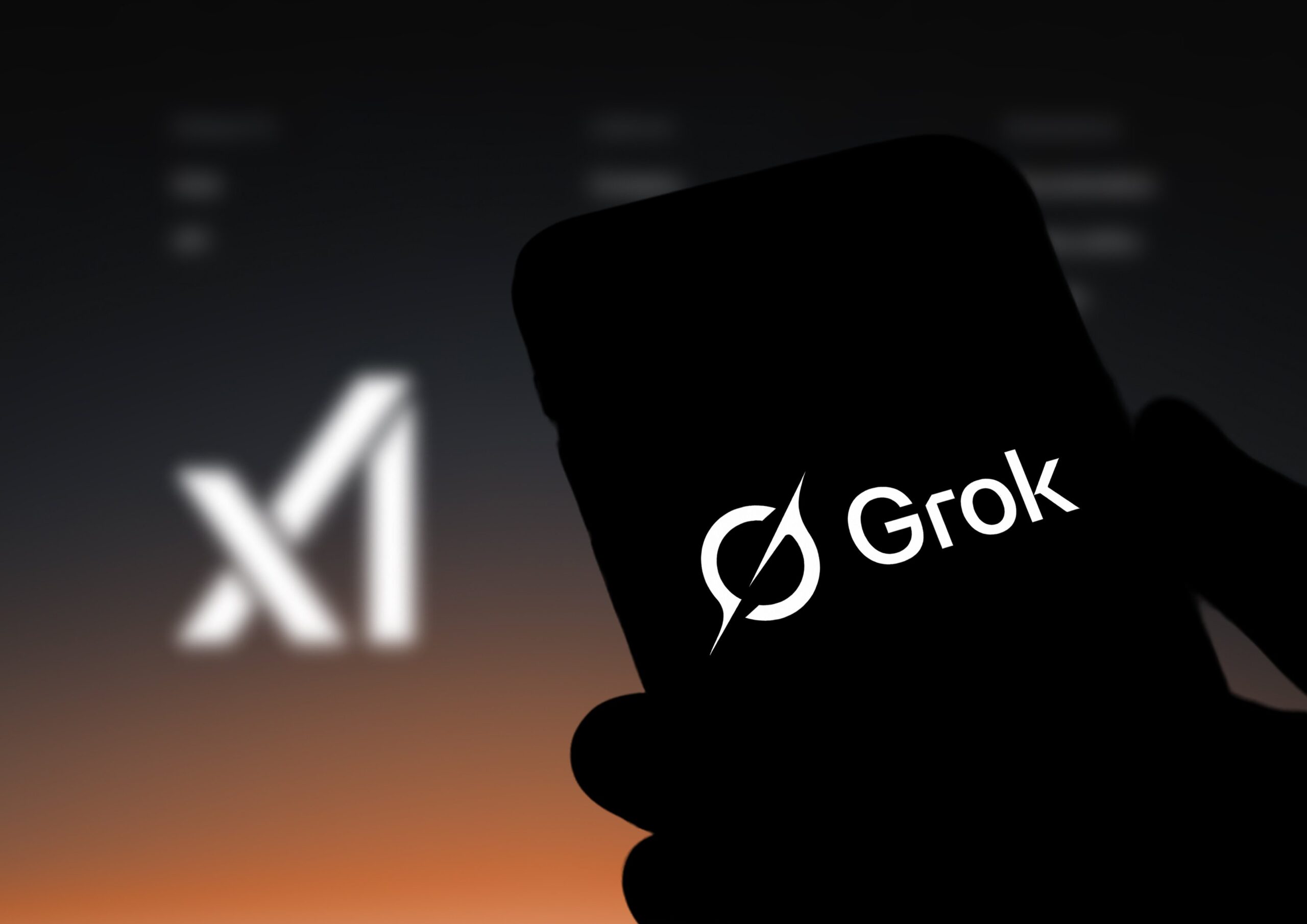 A hand holding a phone displaying the Grok logo. 