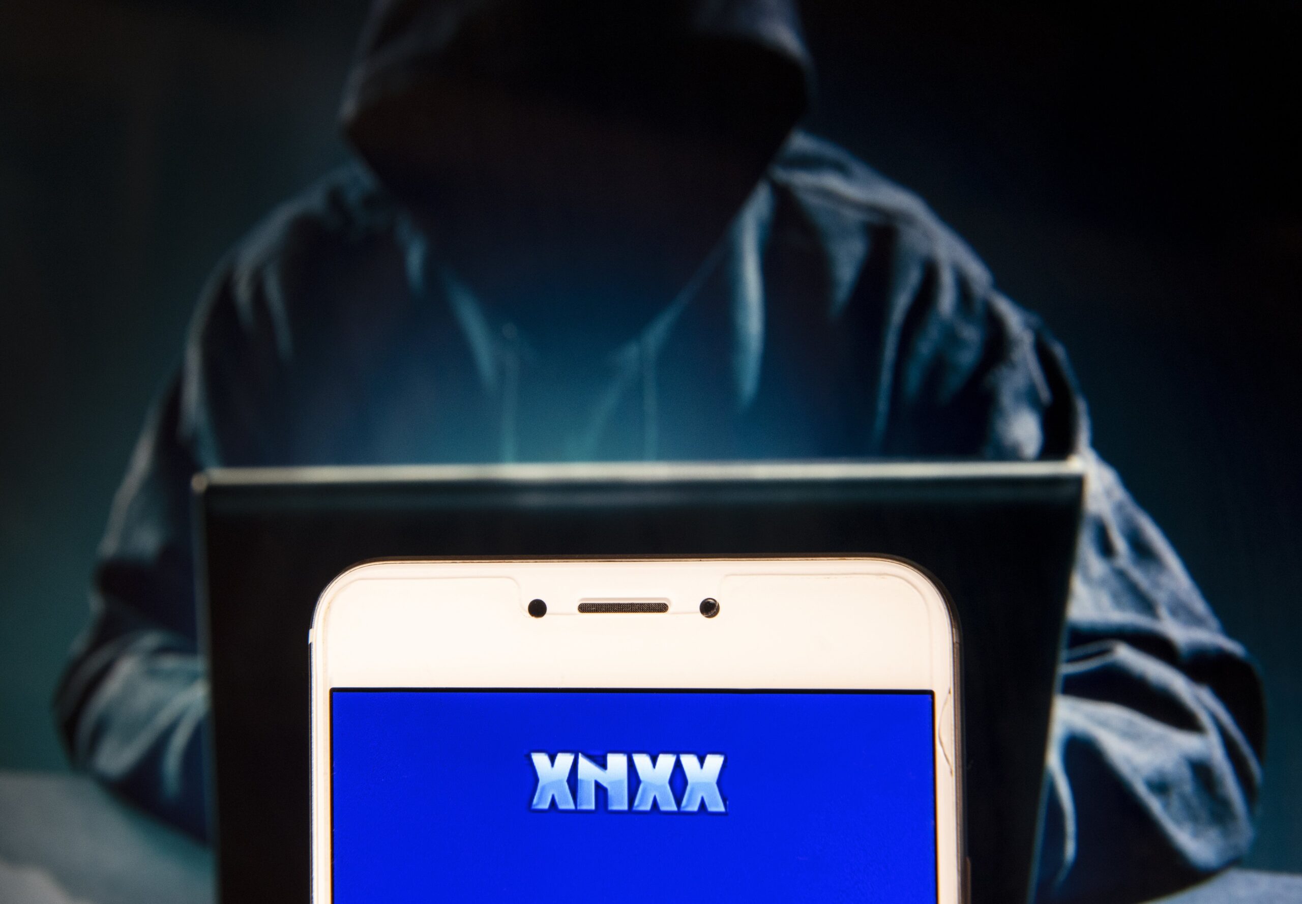 In this photo illustration, the Pornographic video sharing and viewing websites Xnxx logo is seen displayed on an Android mobile device with a figure of hacker in the background
