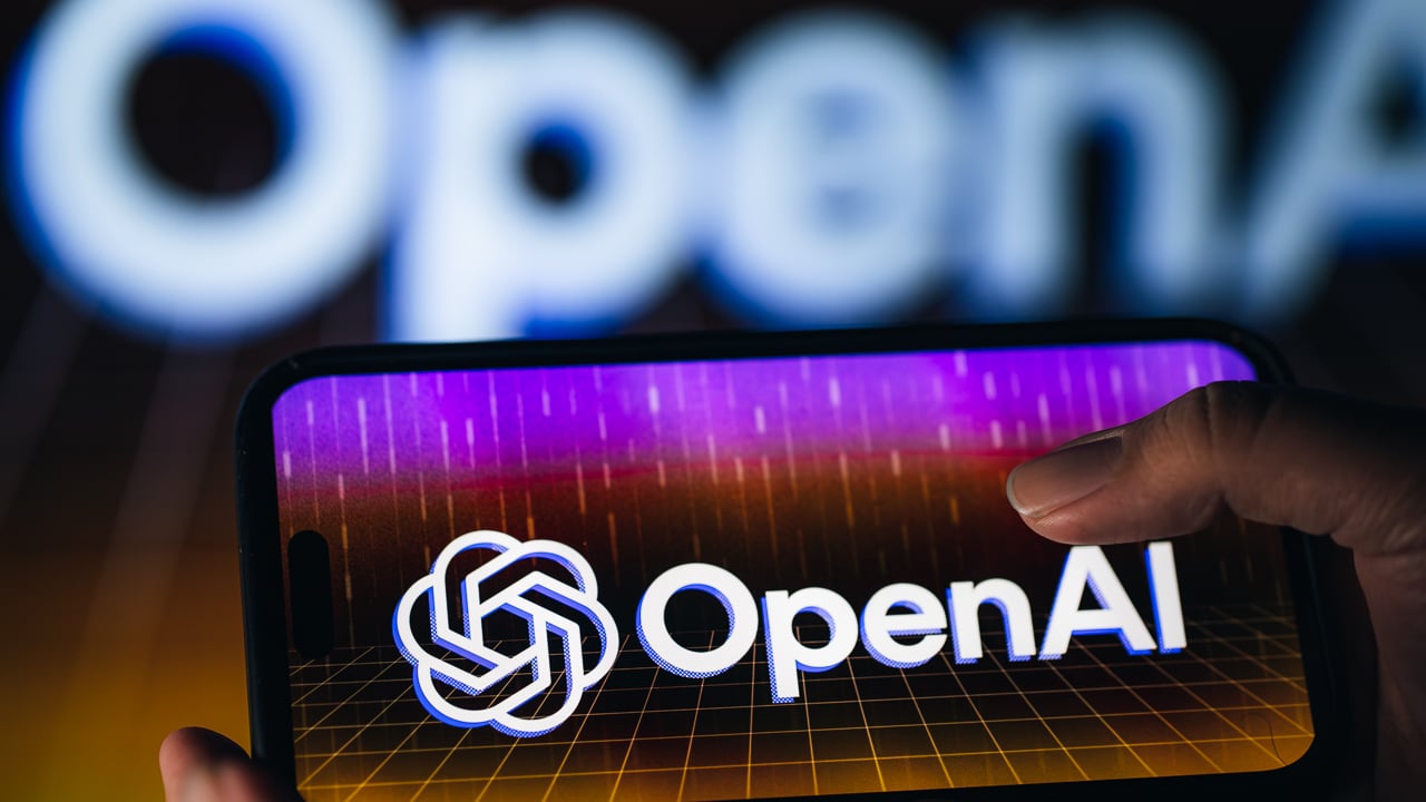A thumb taps on a phone screen displaying a colorful OpenAI logo.