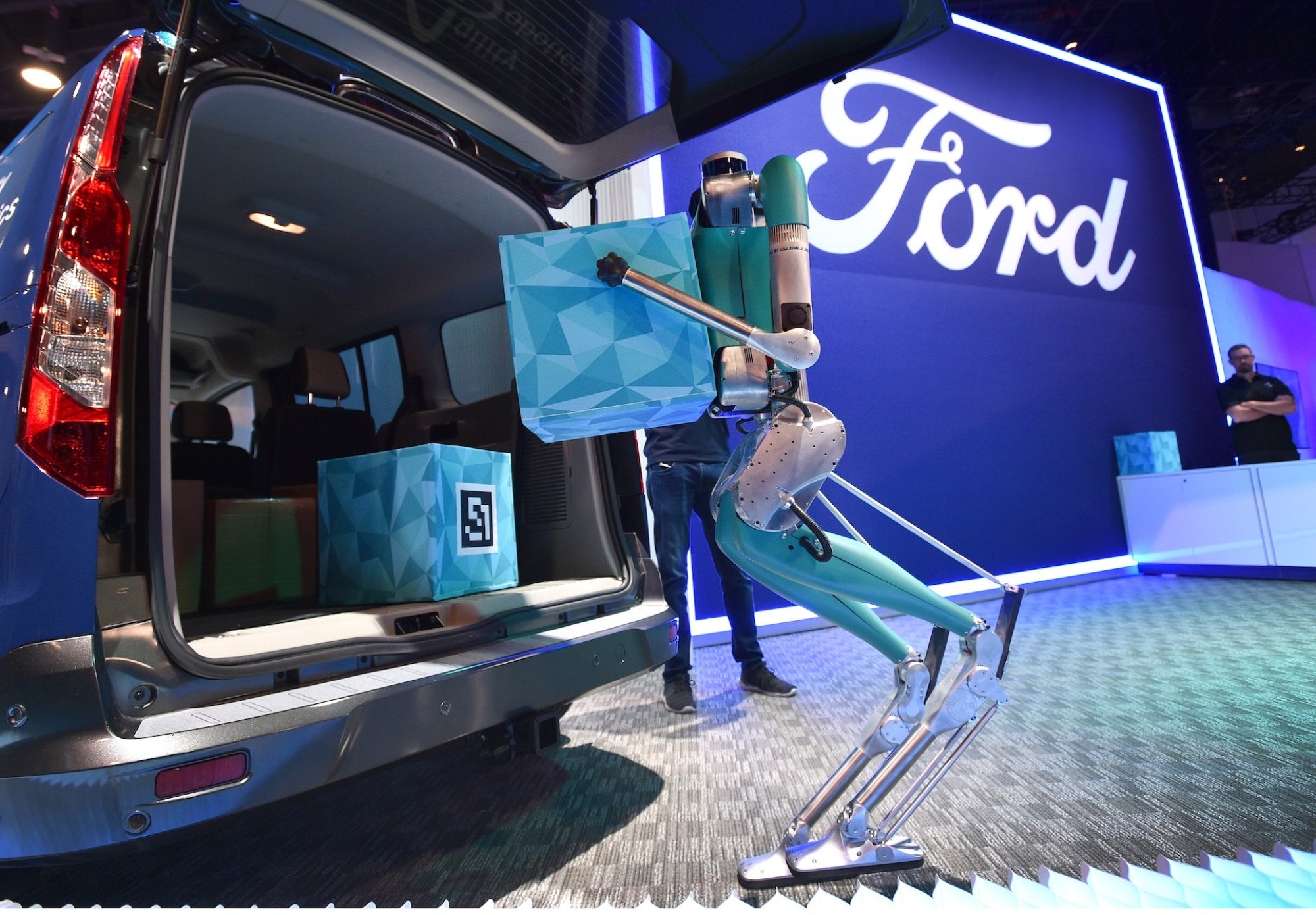 A robot unloads boxes from the back of a truck with a Ford logo in the background