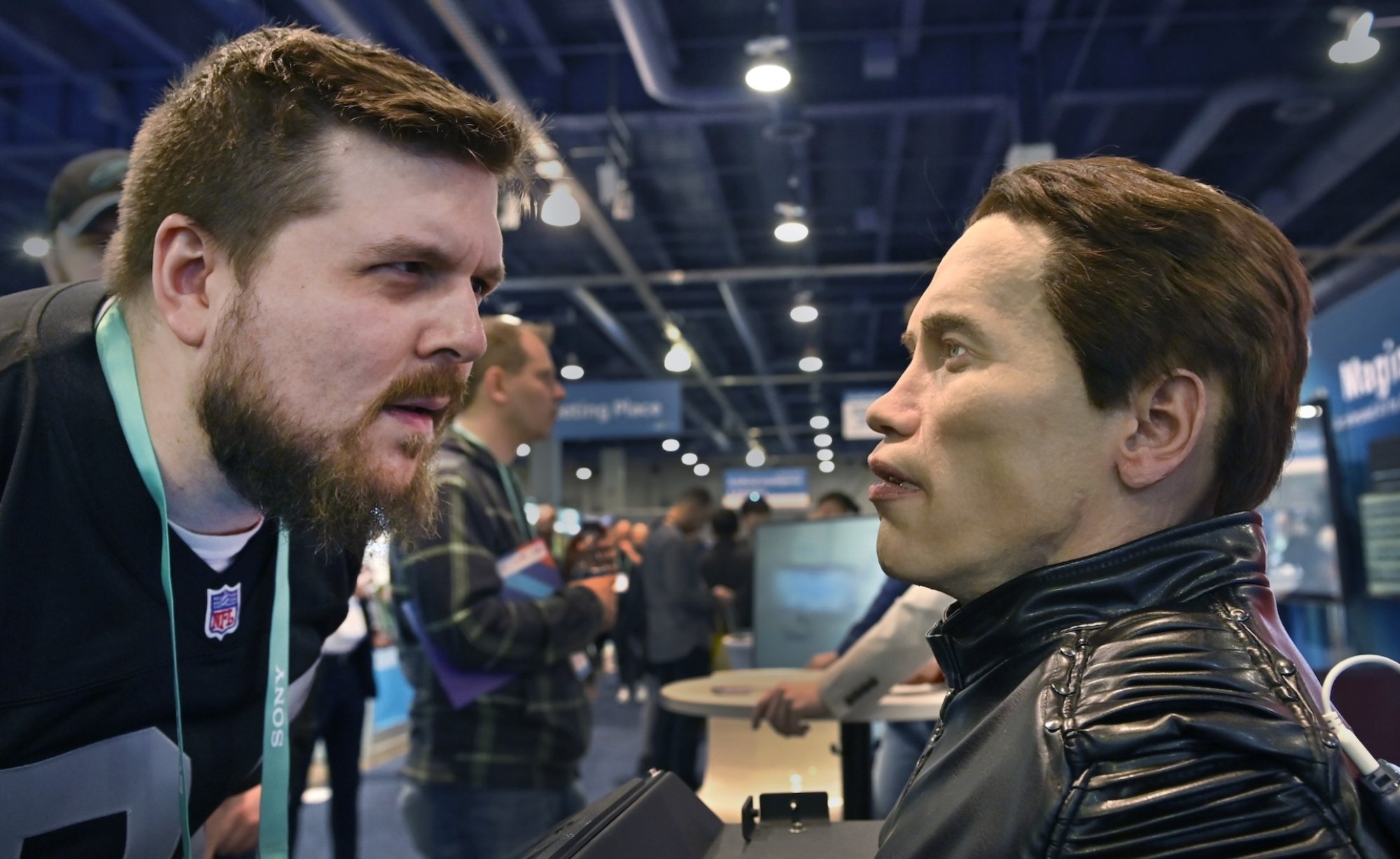 A man with a beard stares at a robot that looks like Arnold Schwarzenegger