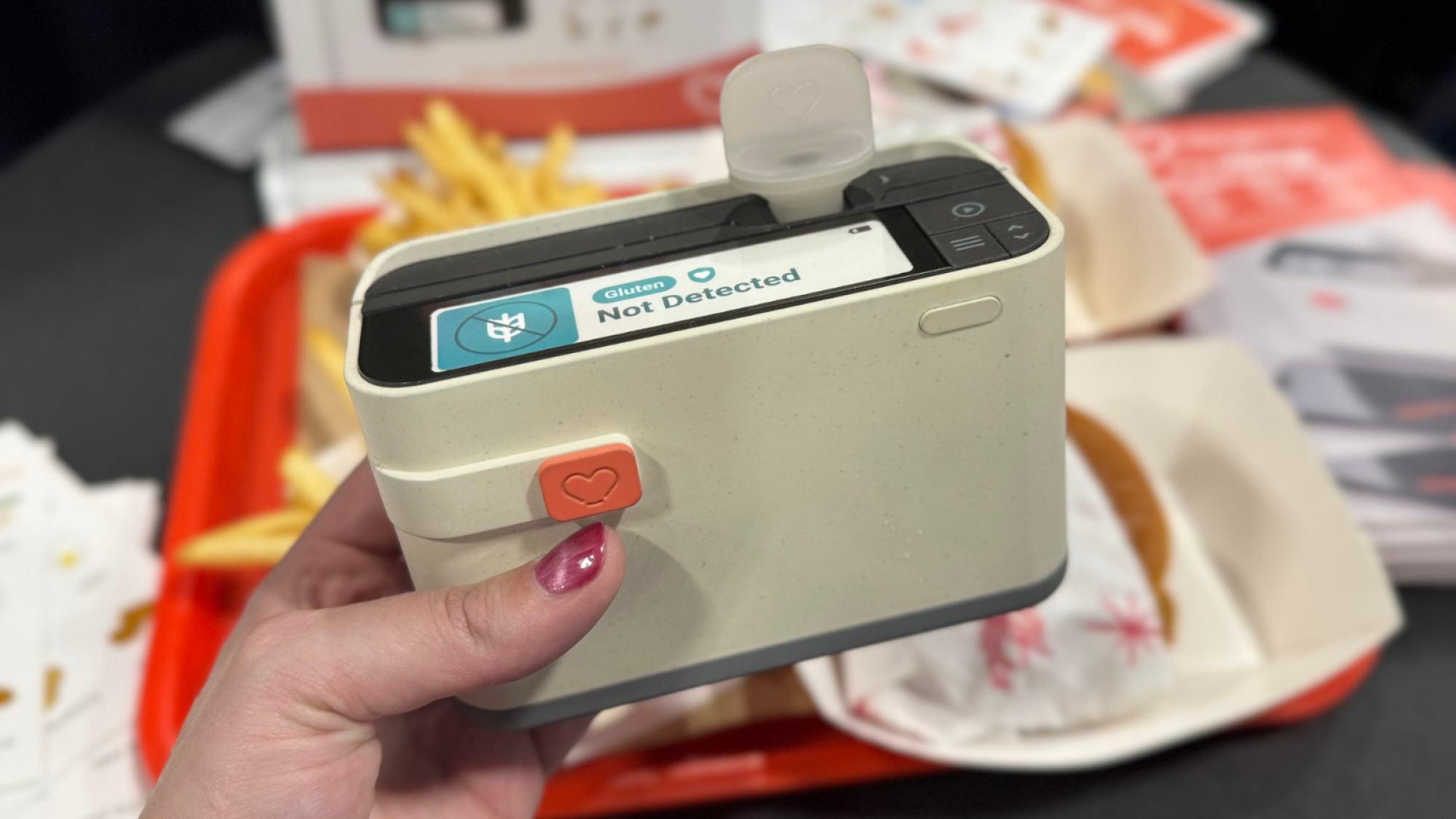 a close-up of a woman holding the allergen alert mini lab in front of a tray of burgers and fries