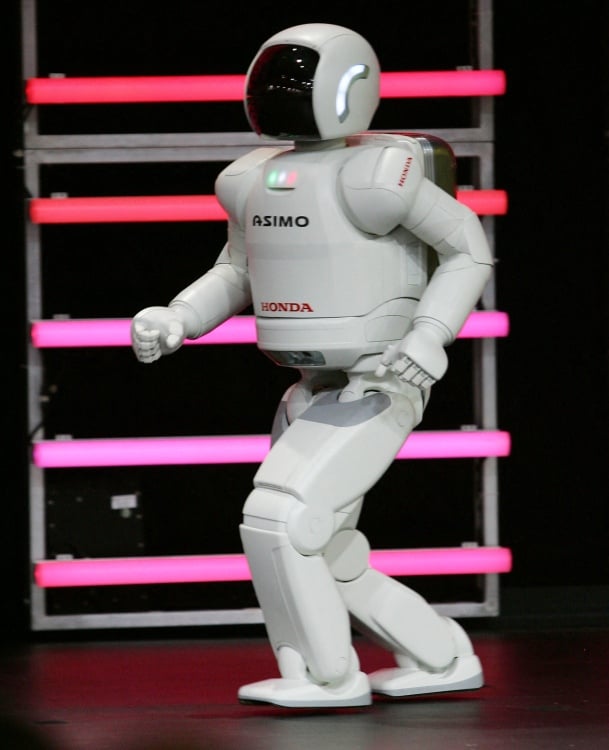 A humanoid robot in a walking stance in front of neon bars