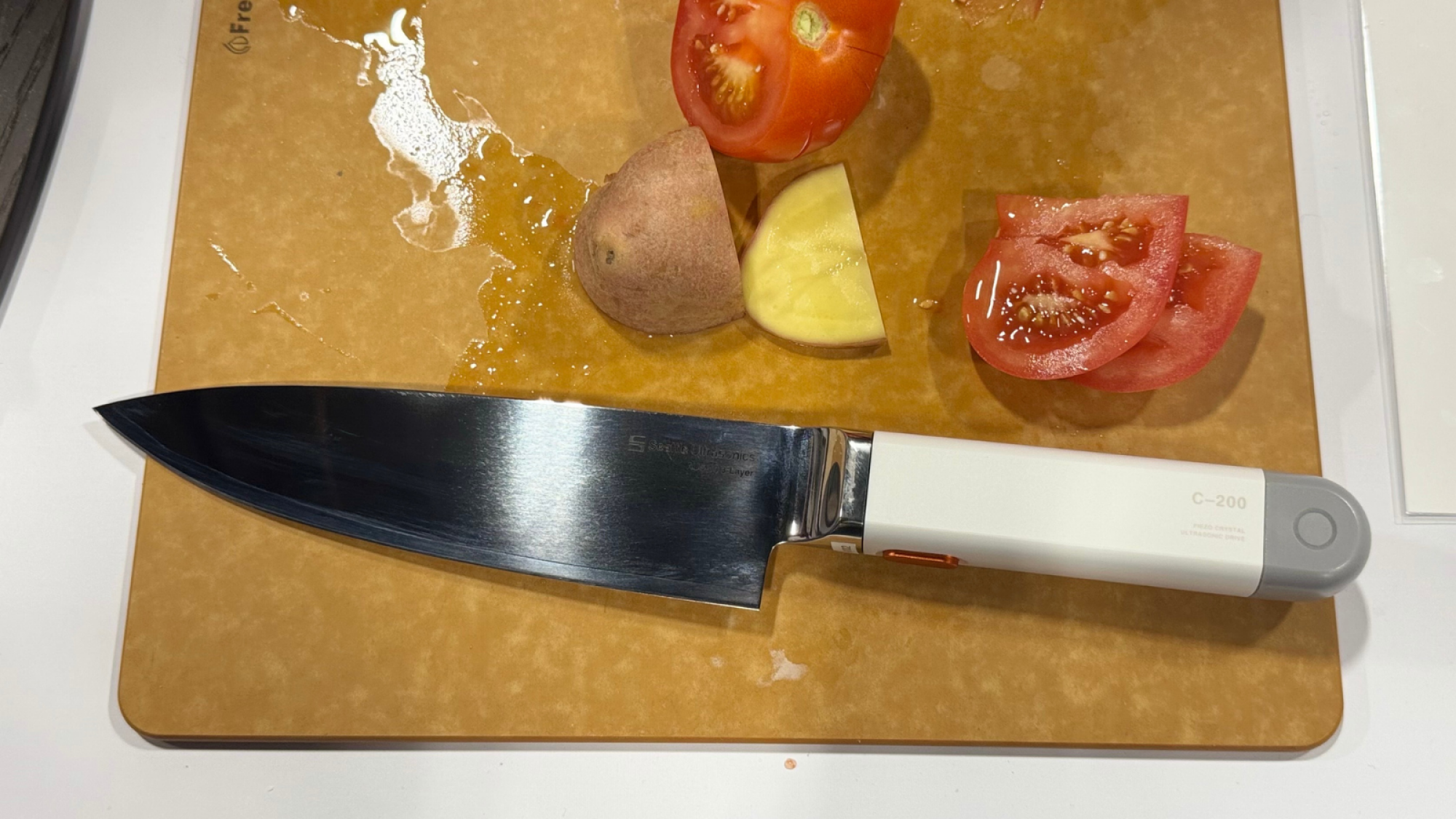 the Seattle Ultrasonics C-200 UltraSonic Chef's Knife on a cutting board next to potatoes and tomatoes