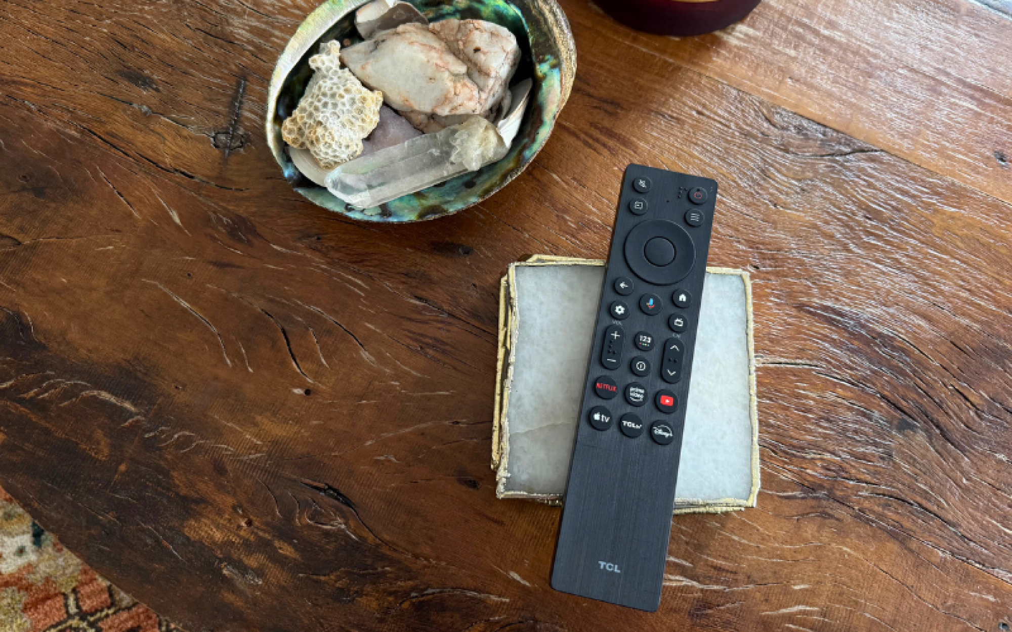 TCL TV remote, coasters, and bowl of crystals laying on wooden coffee table