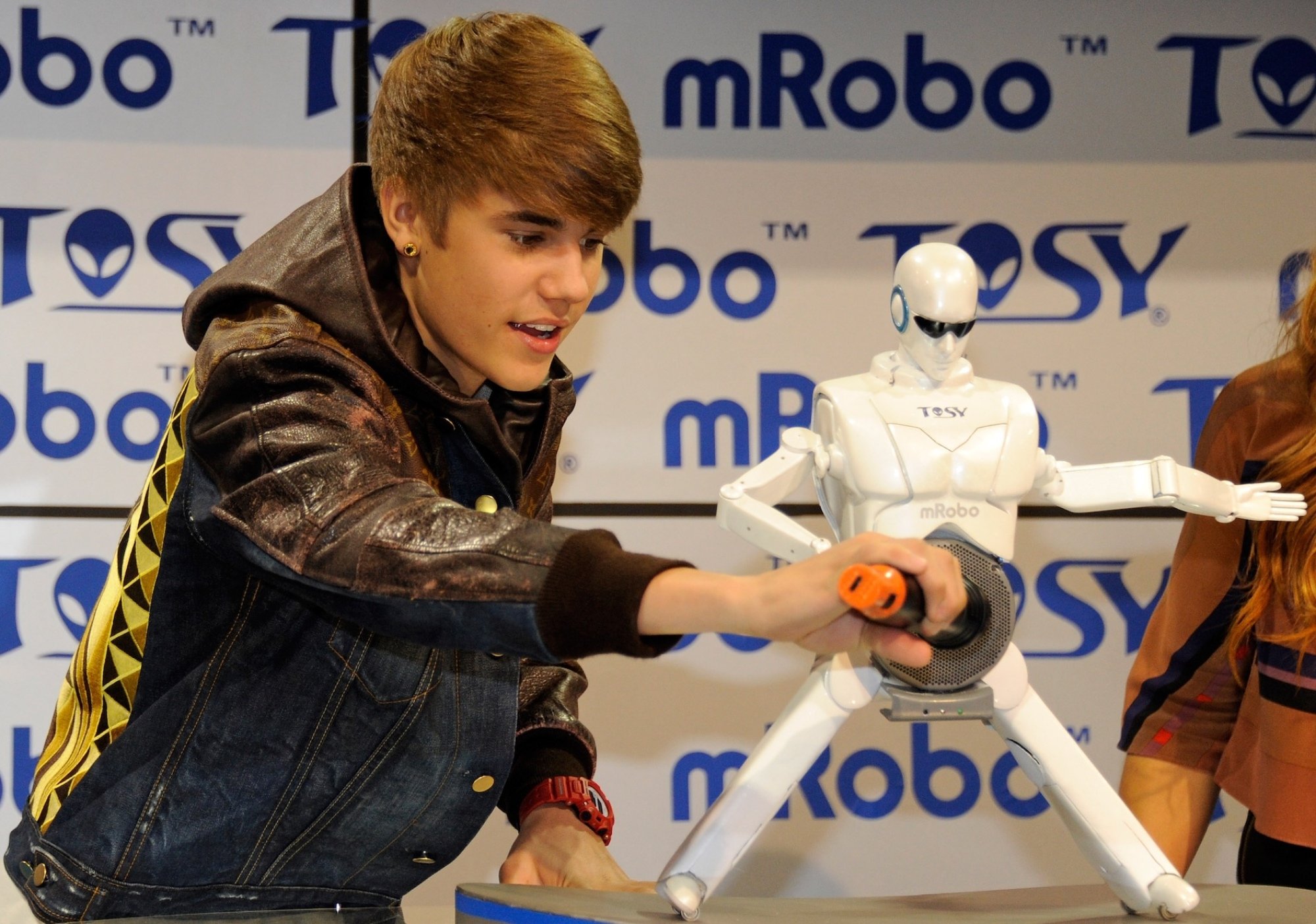 Justin Bieber points a microphone at a robot with a speaker