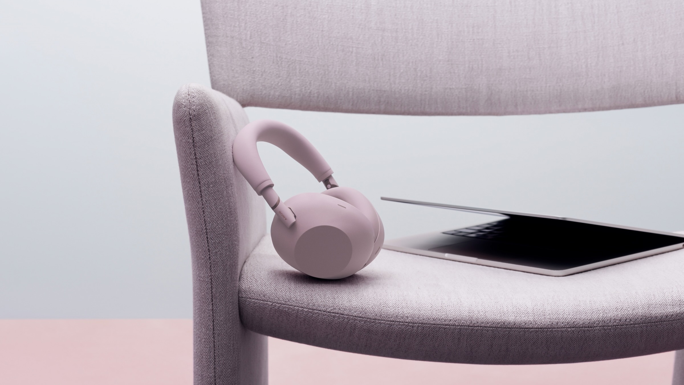 the sony XM6 headphones in sand pink sit on a chair with a laptop in a white room