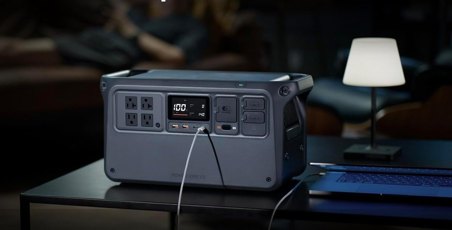 DJI Power 1000 V2 portable power station sits on a tabletop, powering up a lamp and charging a laptop