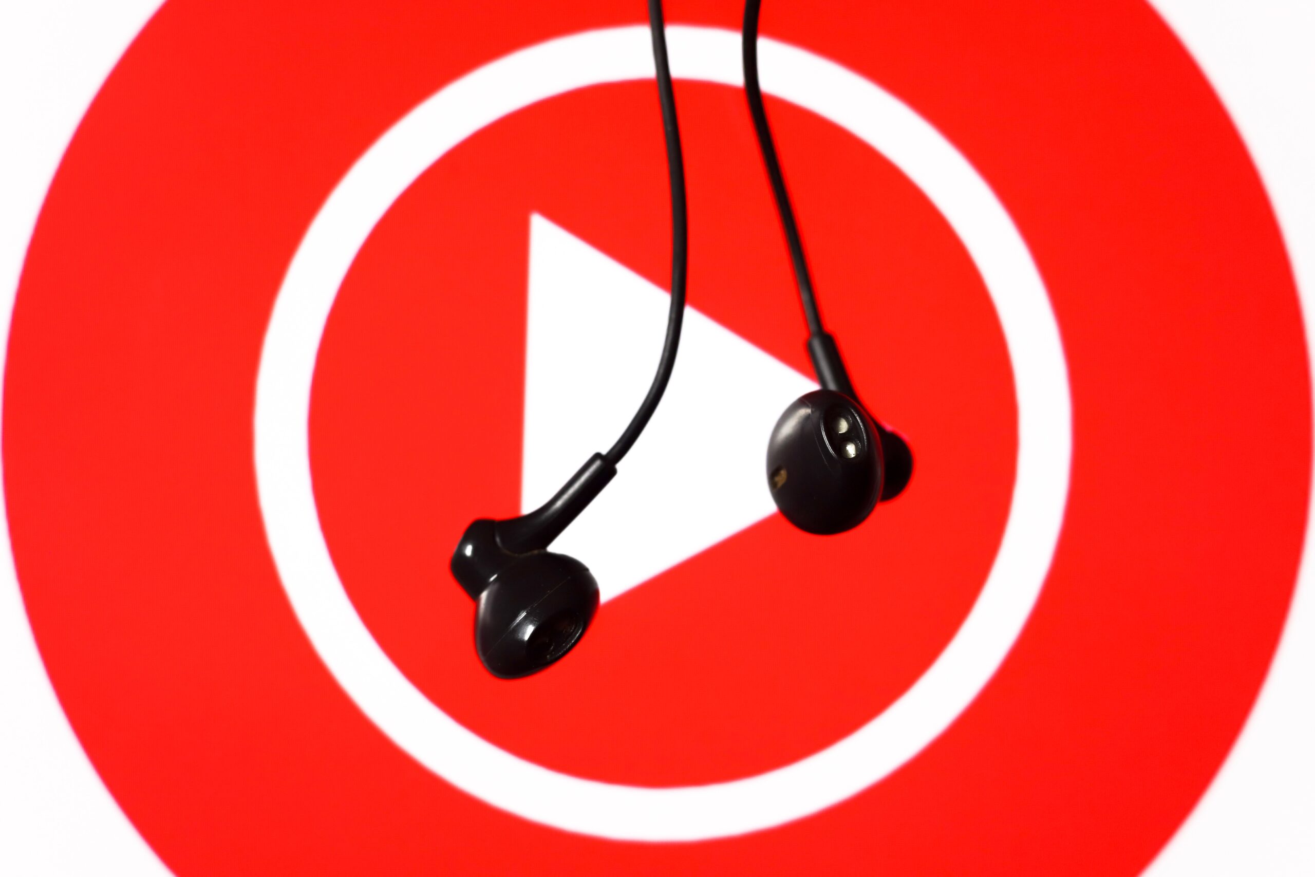 A pair of earbuds dangling in front of a large YouTube Music logo.