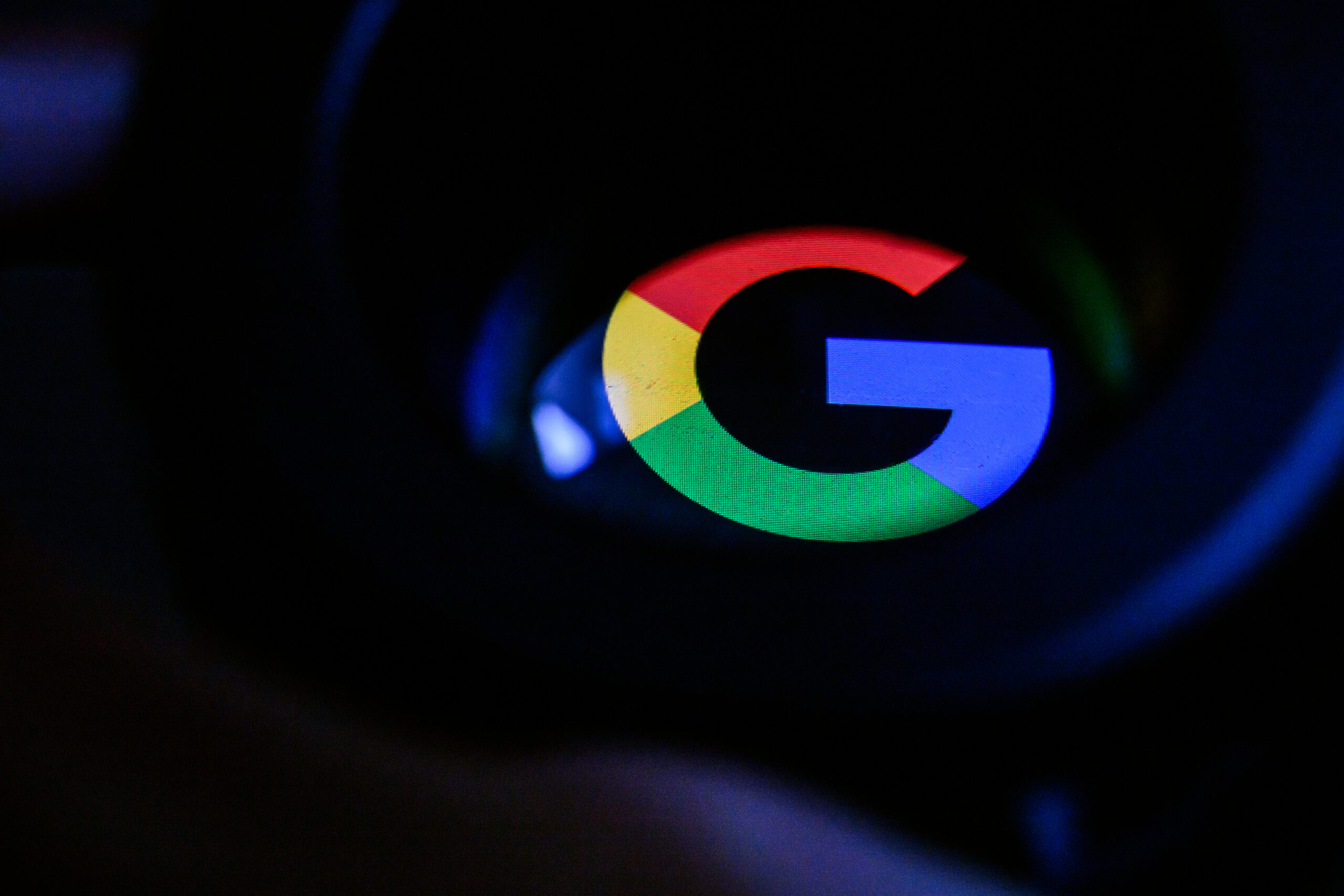 A Google logo reflected in a dark blackish glass. 
