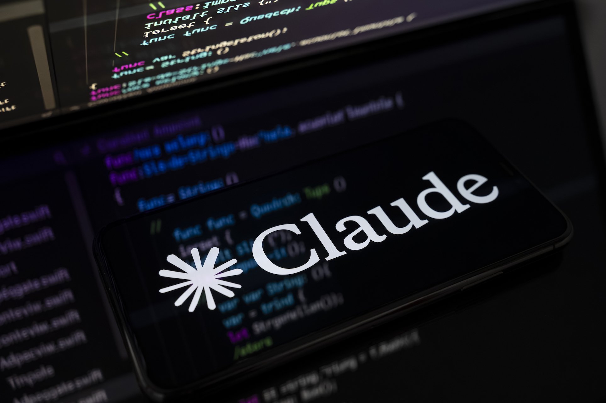 Claude logo on screen with coding in the background, on screen.