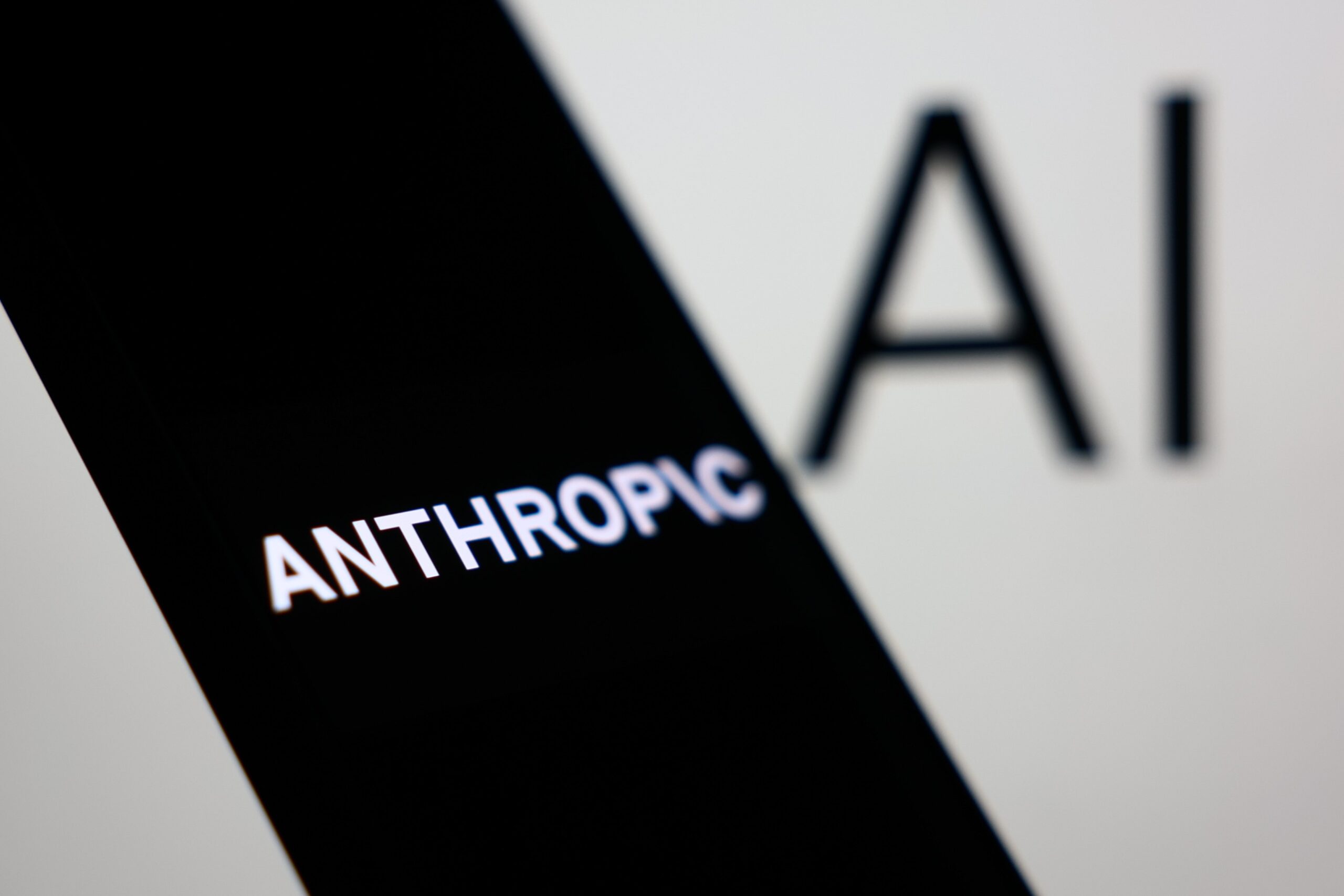 Anthropic logo displayed on a phone screen and AI sign displayed on a screen