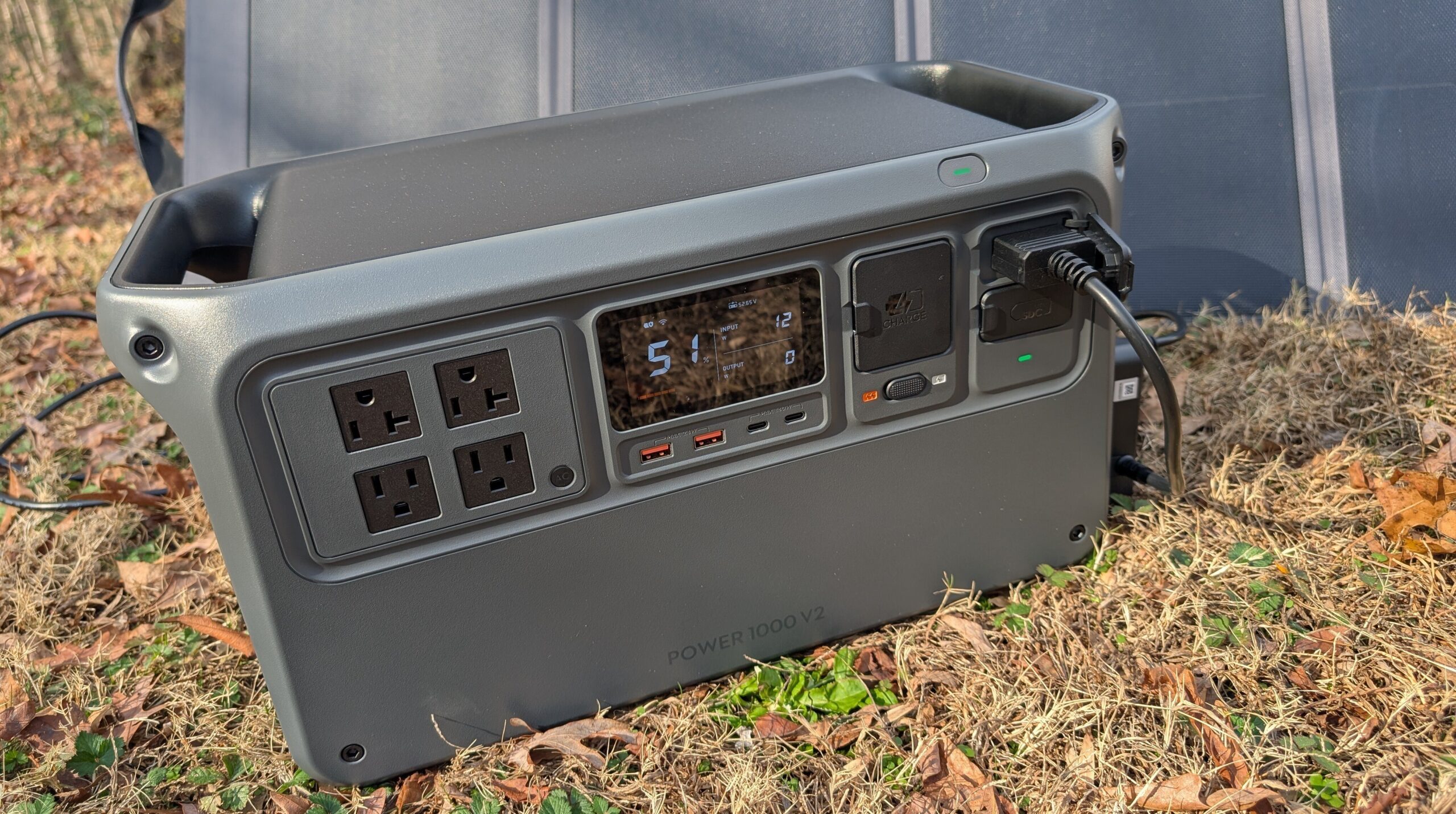 the DJI power 1000 v2 outside sitting in brown grass with a solar panel behind it on a sunny day