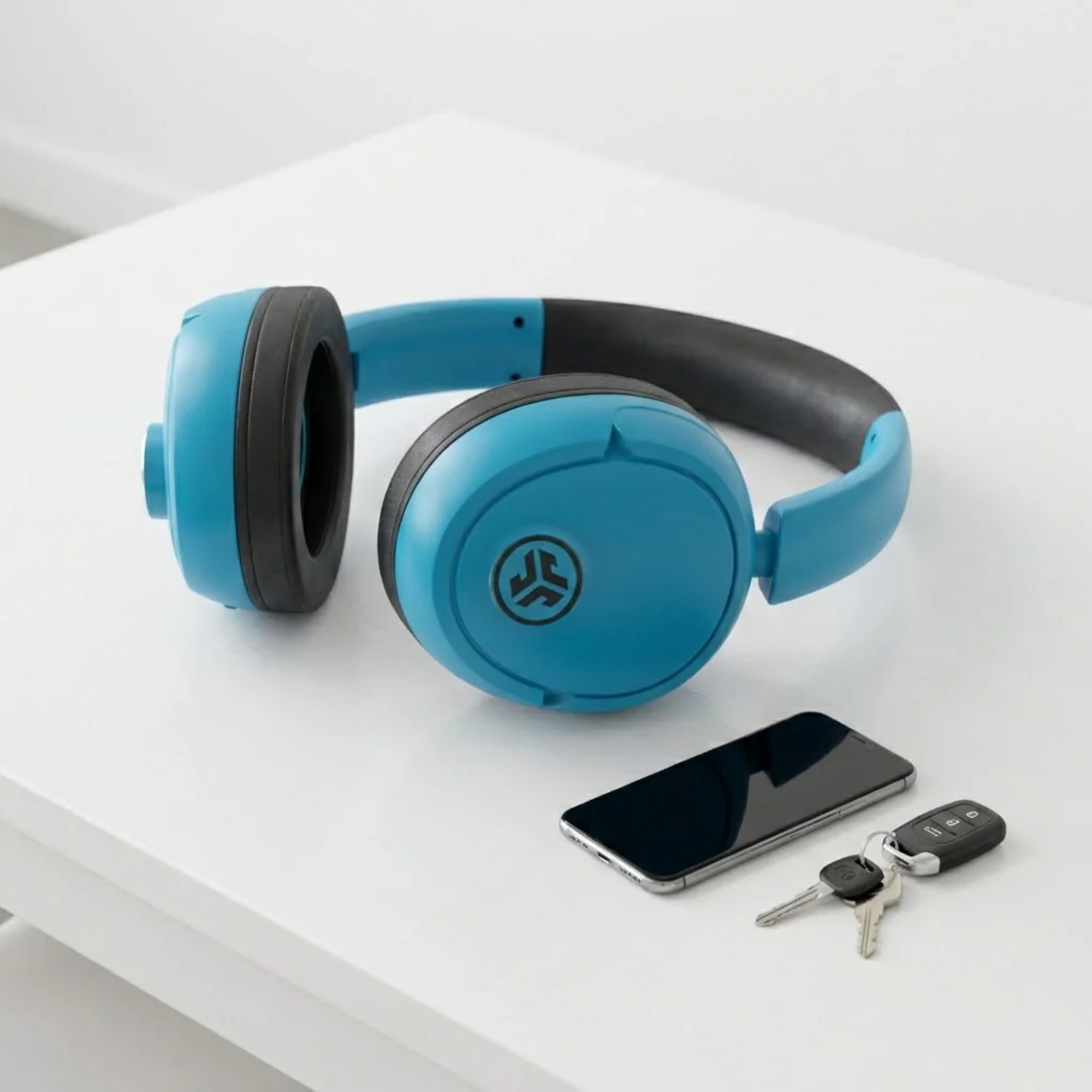 the jlab blue xl speaker headphones next to a phone and keys