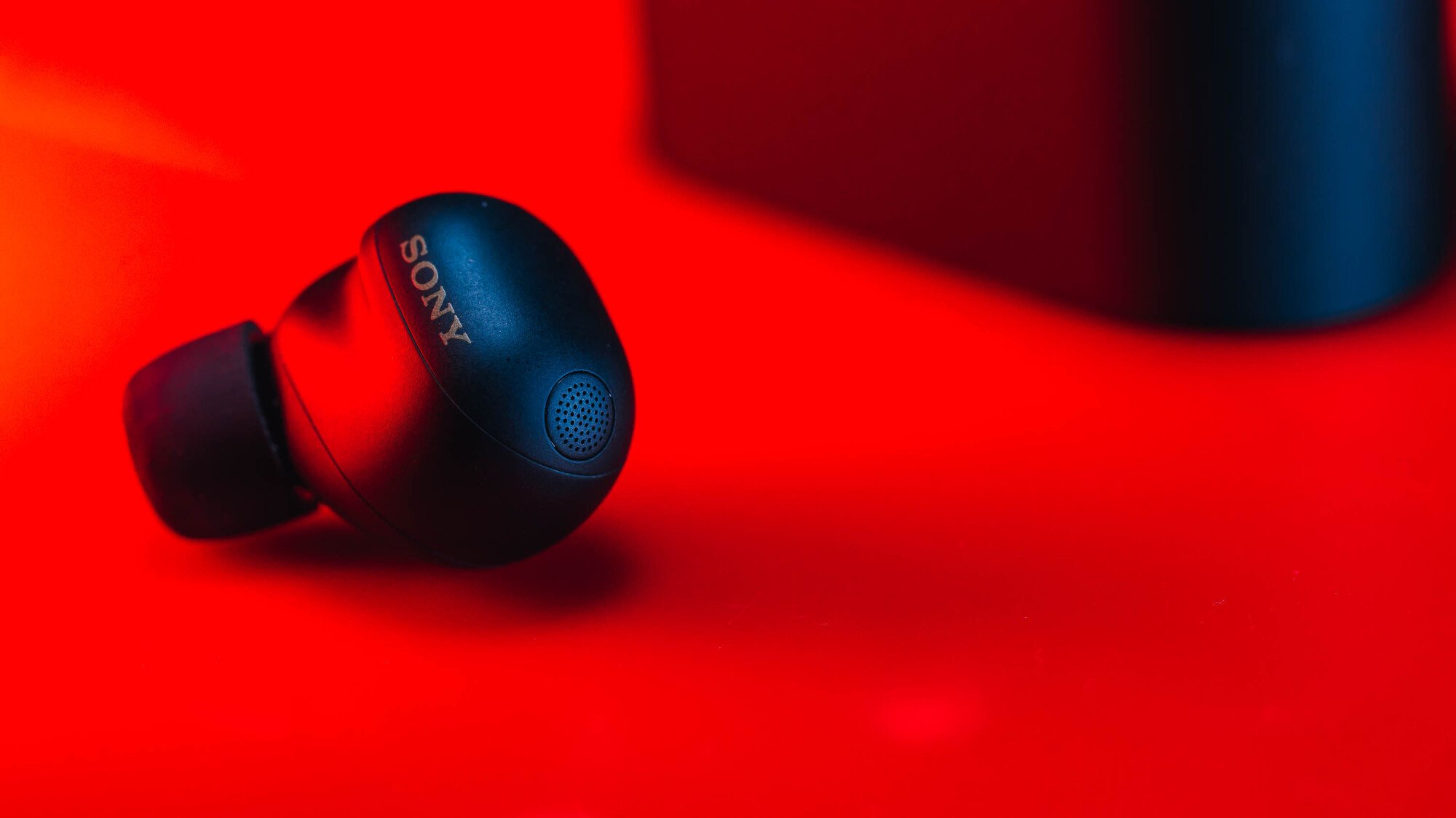 close-up portrait of sony xm6 earbud with charging case in background