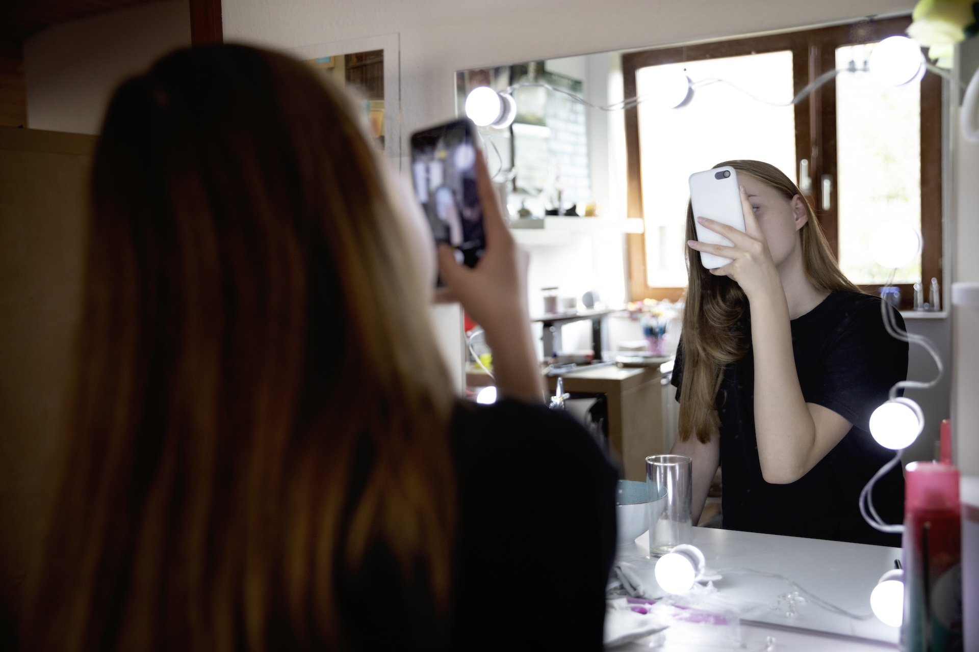 Teen girl takes selfie in front of a bathroom mirror.