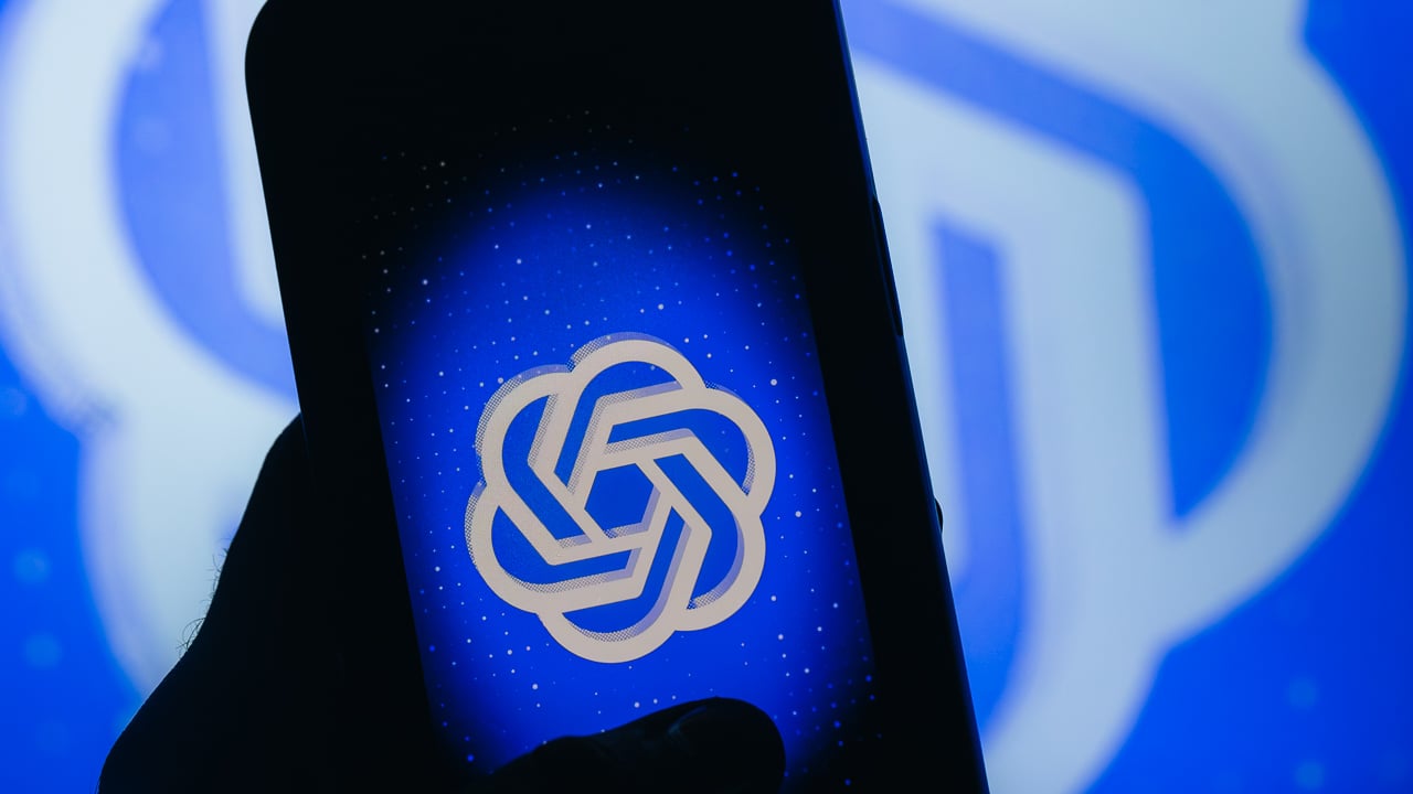 A hand in shadows holds a glowing phone, displaying a blue ChatGPT logo.