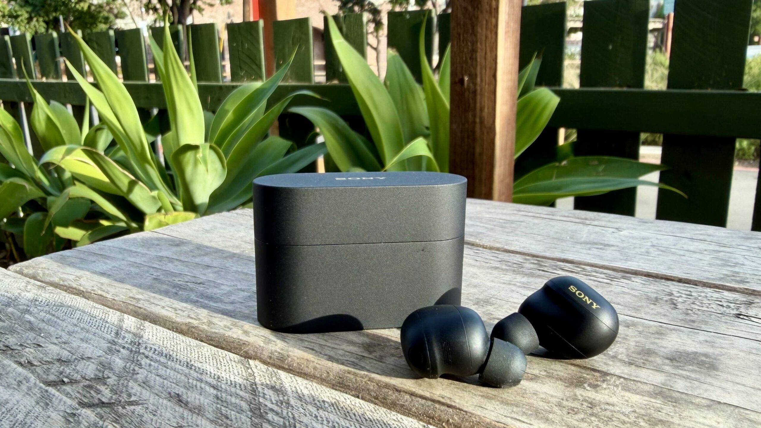 black sony xm6 earbuds and their case on picnic table in outside patio