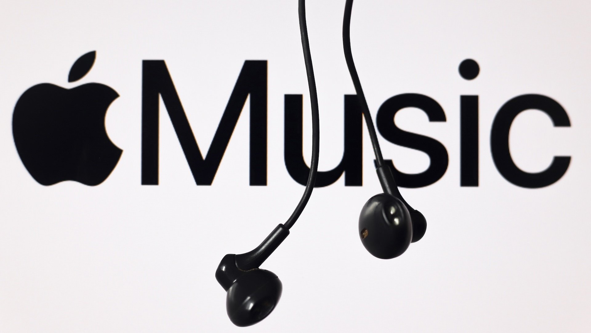 The Apple Music logo sits behind hanging earbuds.