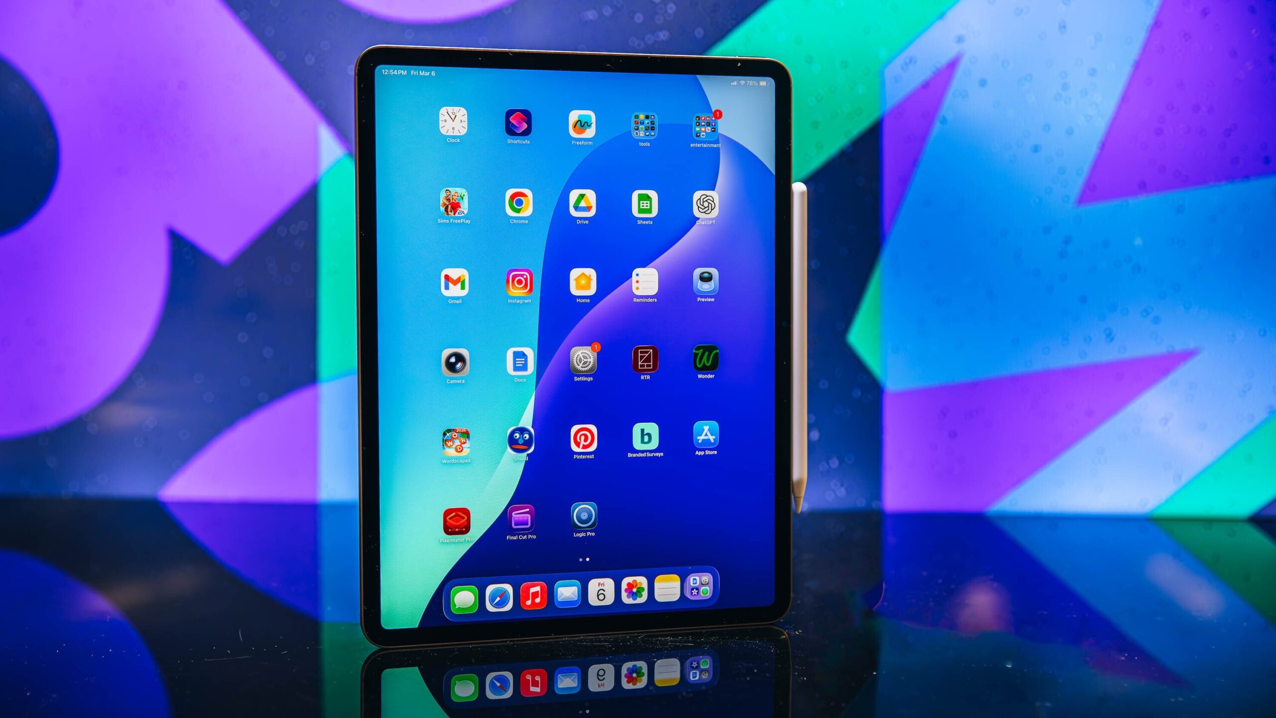 A portrait of Apple's new M4 iPad Air with an Apple Pencil showing the home screen, sitting on a table with a colorful background..