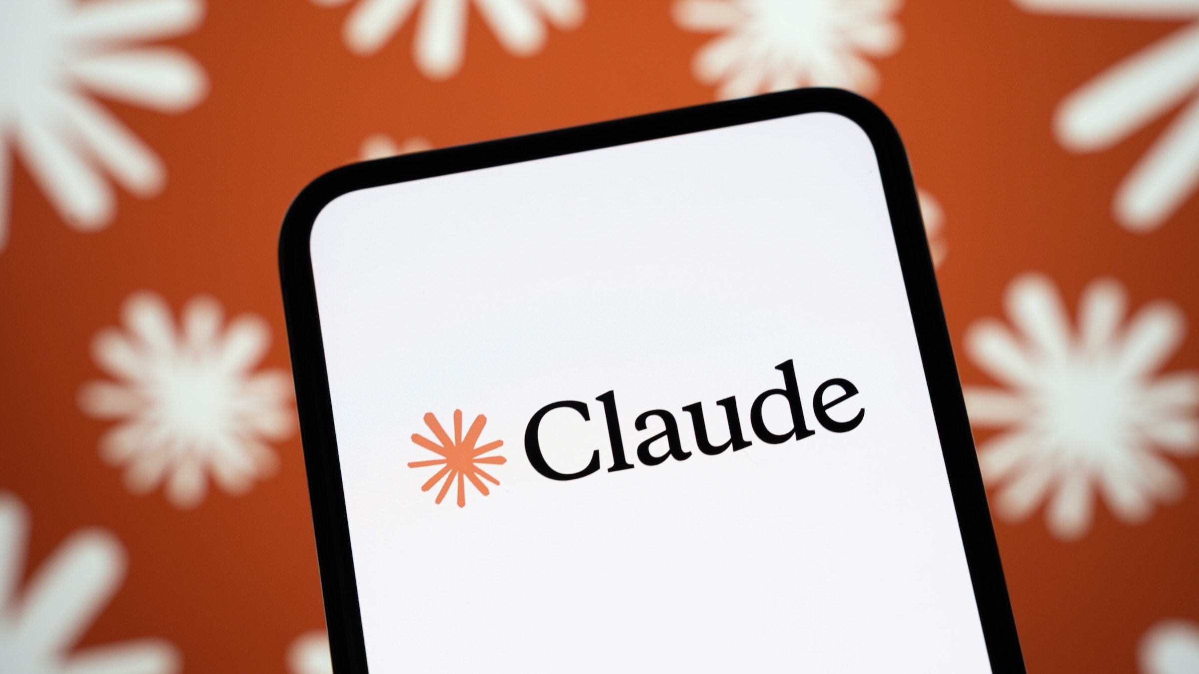 The Claude AI logo is displayed on a smartphone screen with a multitude of Anthropic logos in the background