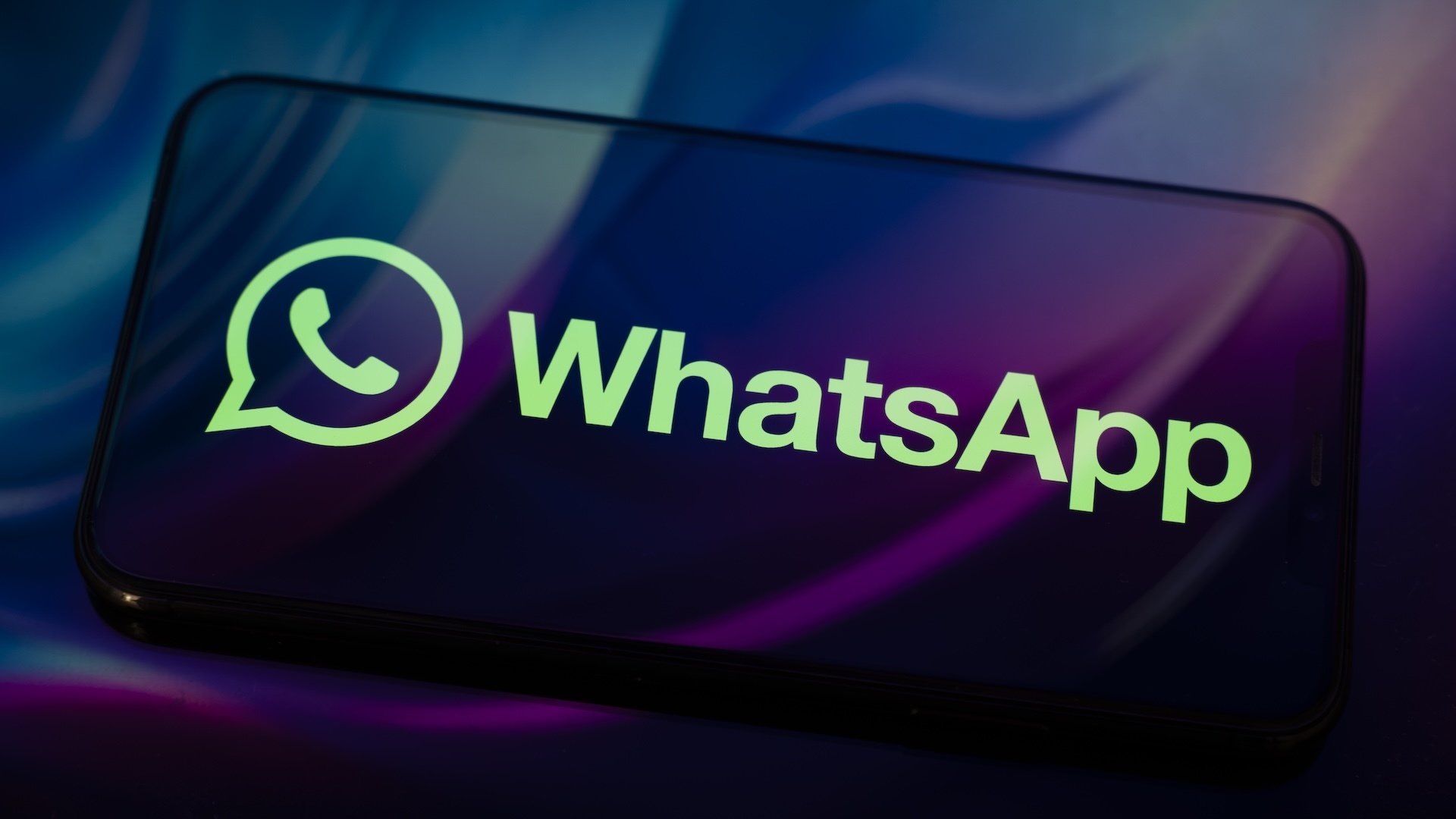 The WhatsApp logo appears on a smartphone reflecting an abstract illustration in blue and purple colors.
