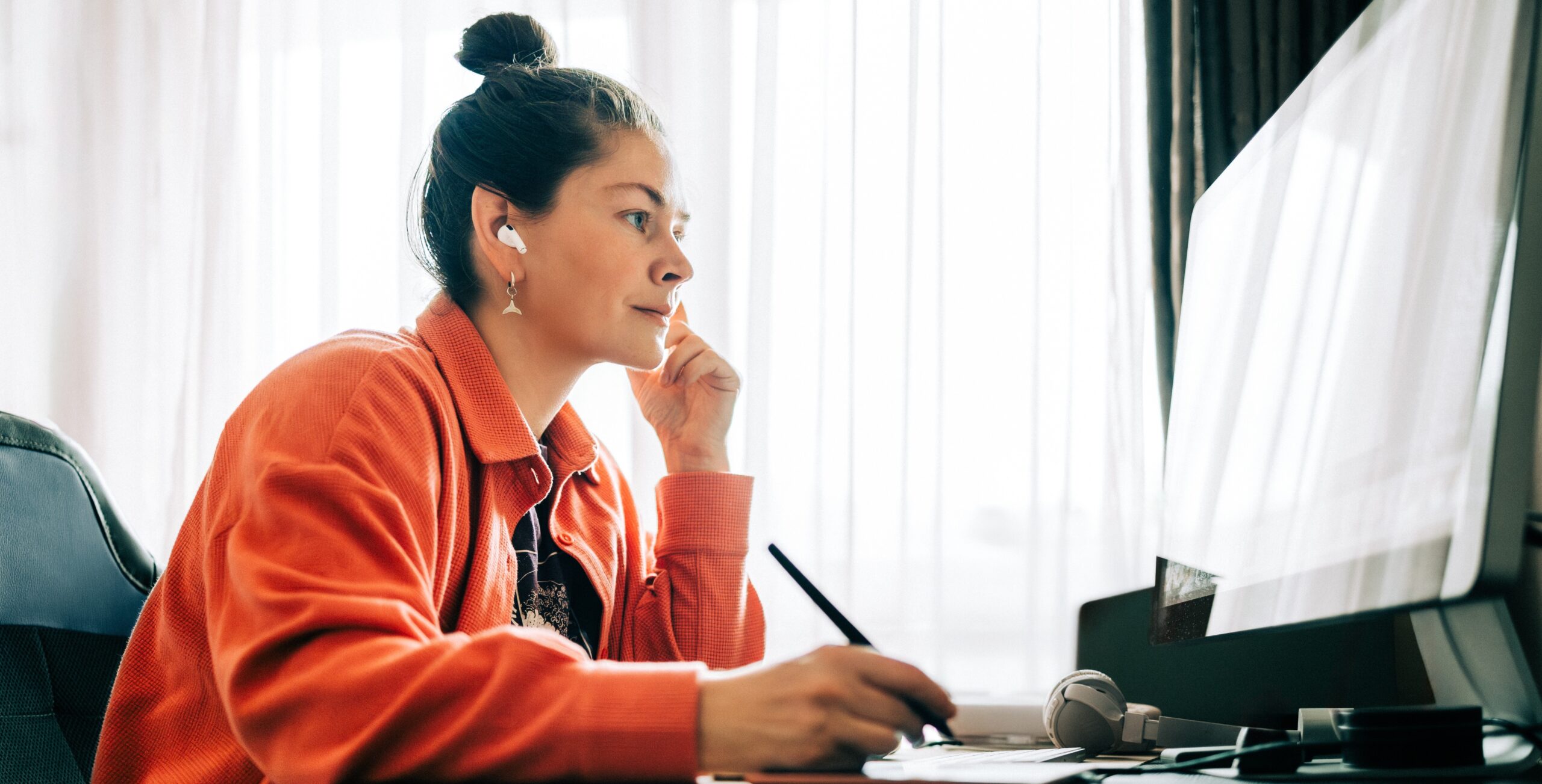 a person sits at a computer looking at the screen with an earbud in the right ear