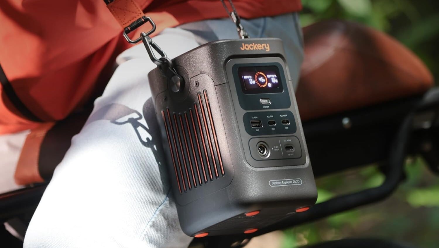 the Jackery Explorer 240D slung over a sholder and sitting on a person's leg while they ride a bicycle