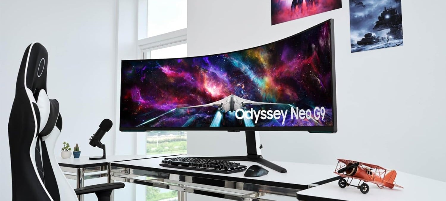 the 57-inch Samsung Odyssey Neo G9 sits on a desk in a white room