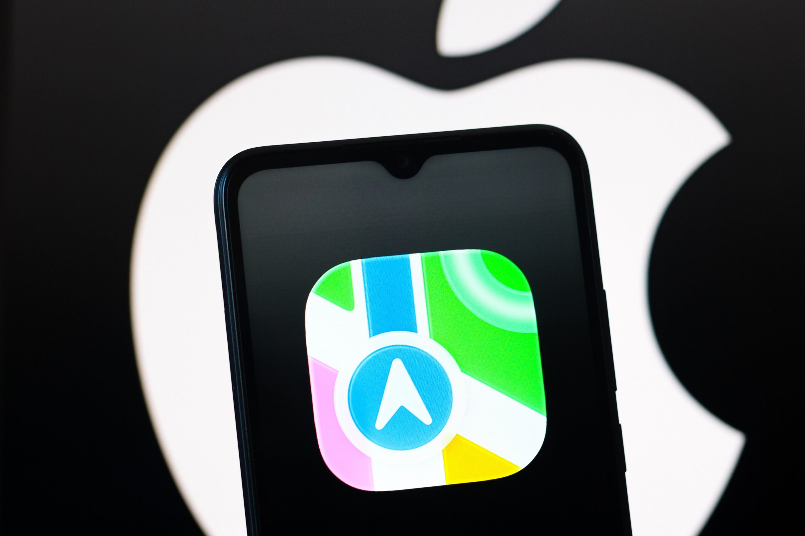 Apple Maps logo on mobile device with Apple logo in the background