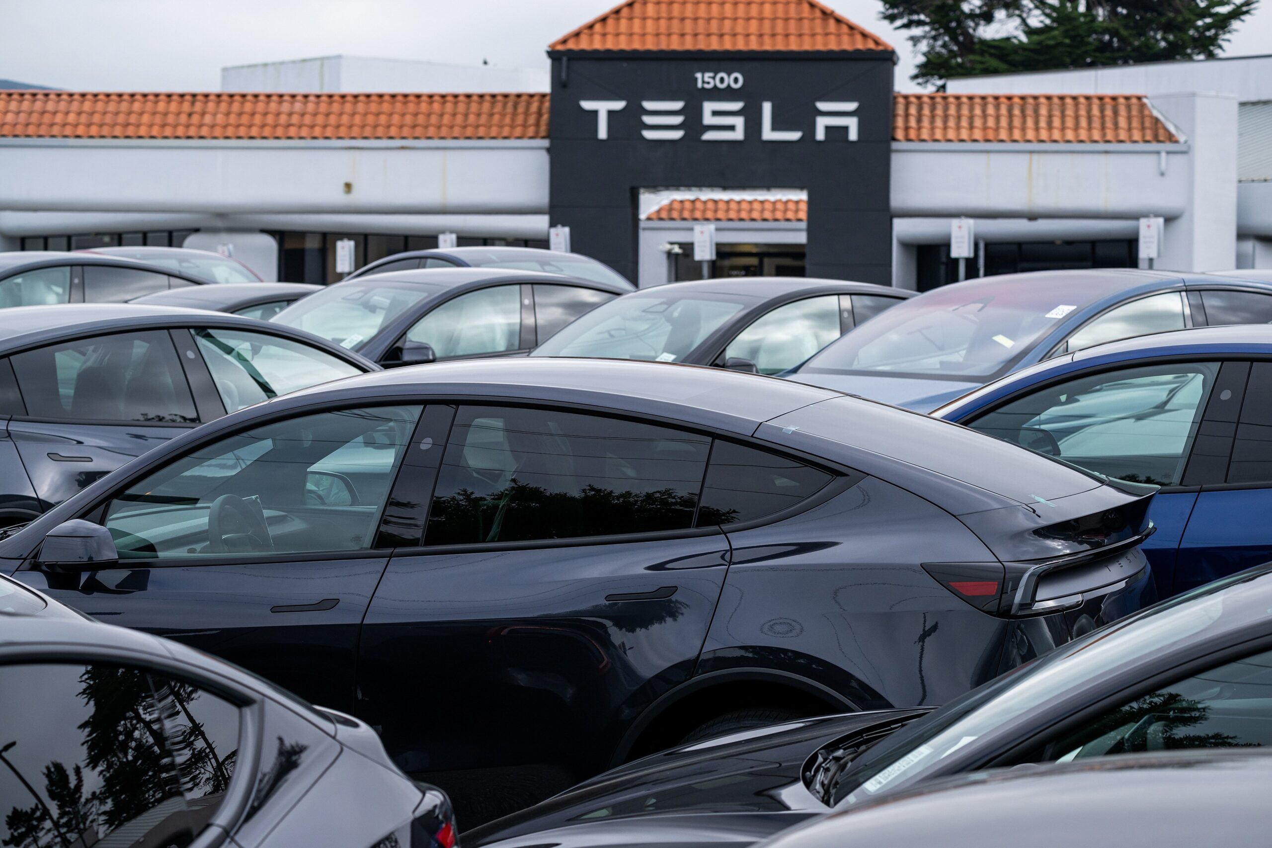 A lot of cars in front of a Tesla dealership building.
