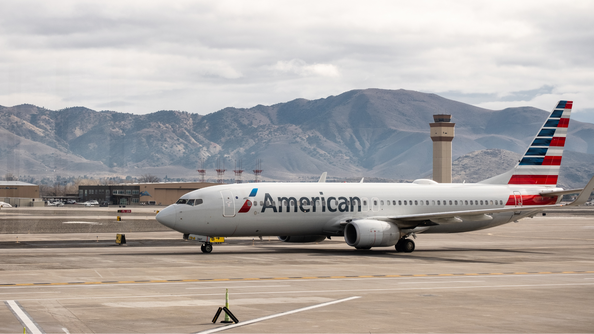 An American Airlines 737-800 taxing at Reno-Tahoe International Airport terminal with the control tower in the background.