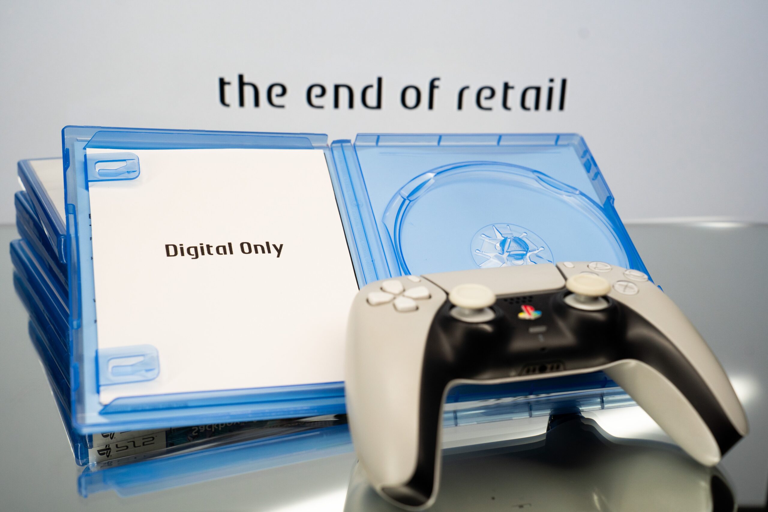 A PlayStation 5 controller and an open, empty retail game case containing a card that reads ''Digital Only'' are seen, with the text ''the end of retail'' displayed on a screen in the background