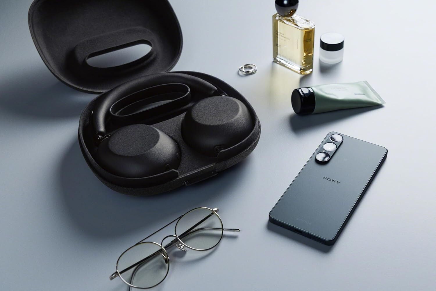 Sony WH-1000X The Collexion headphones in case laying next to glasses, phone, and other accessories