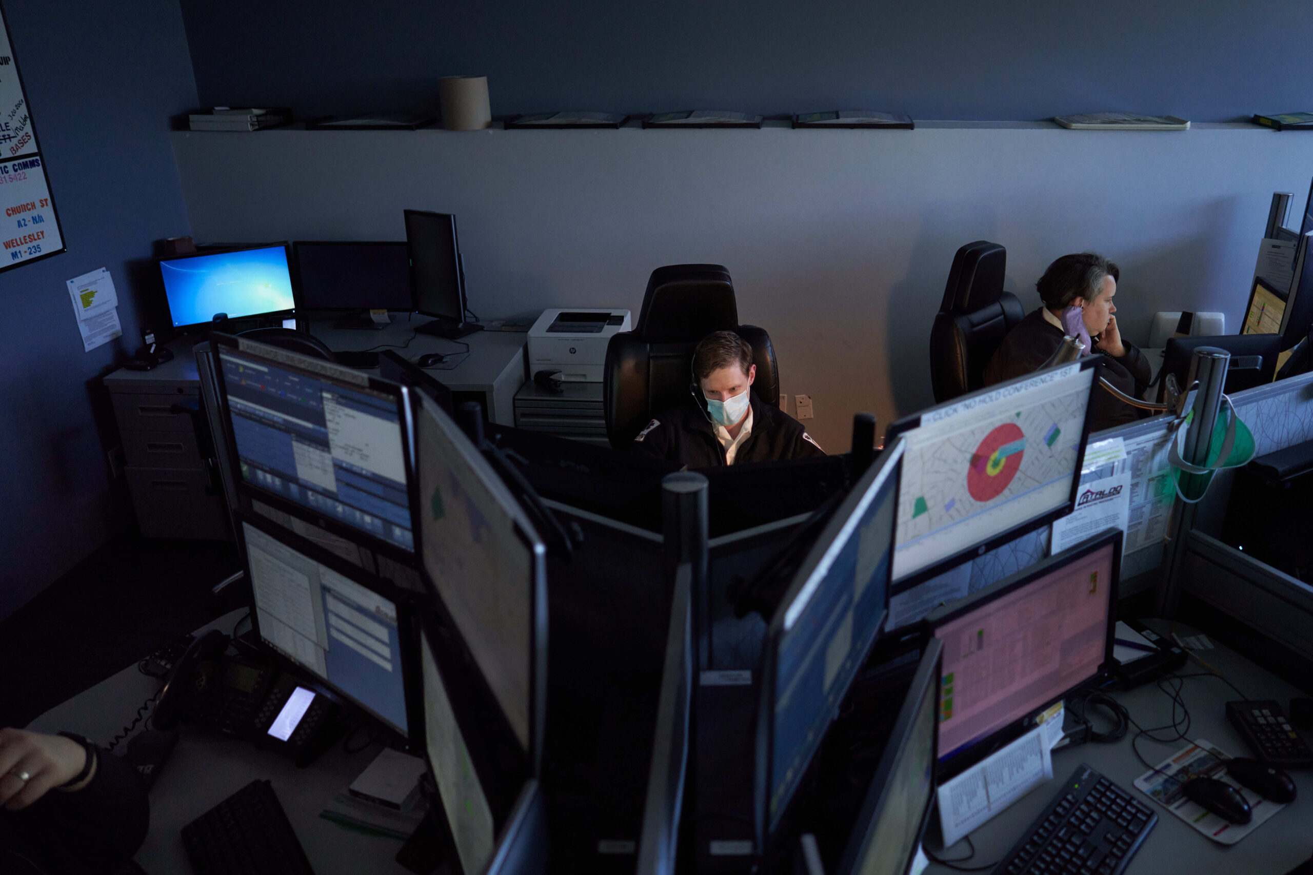 A 911 operator stares at a screen amid a bank of computer screens.