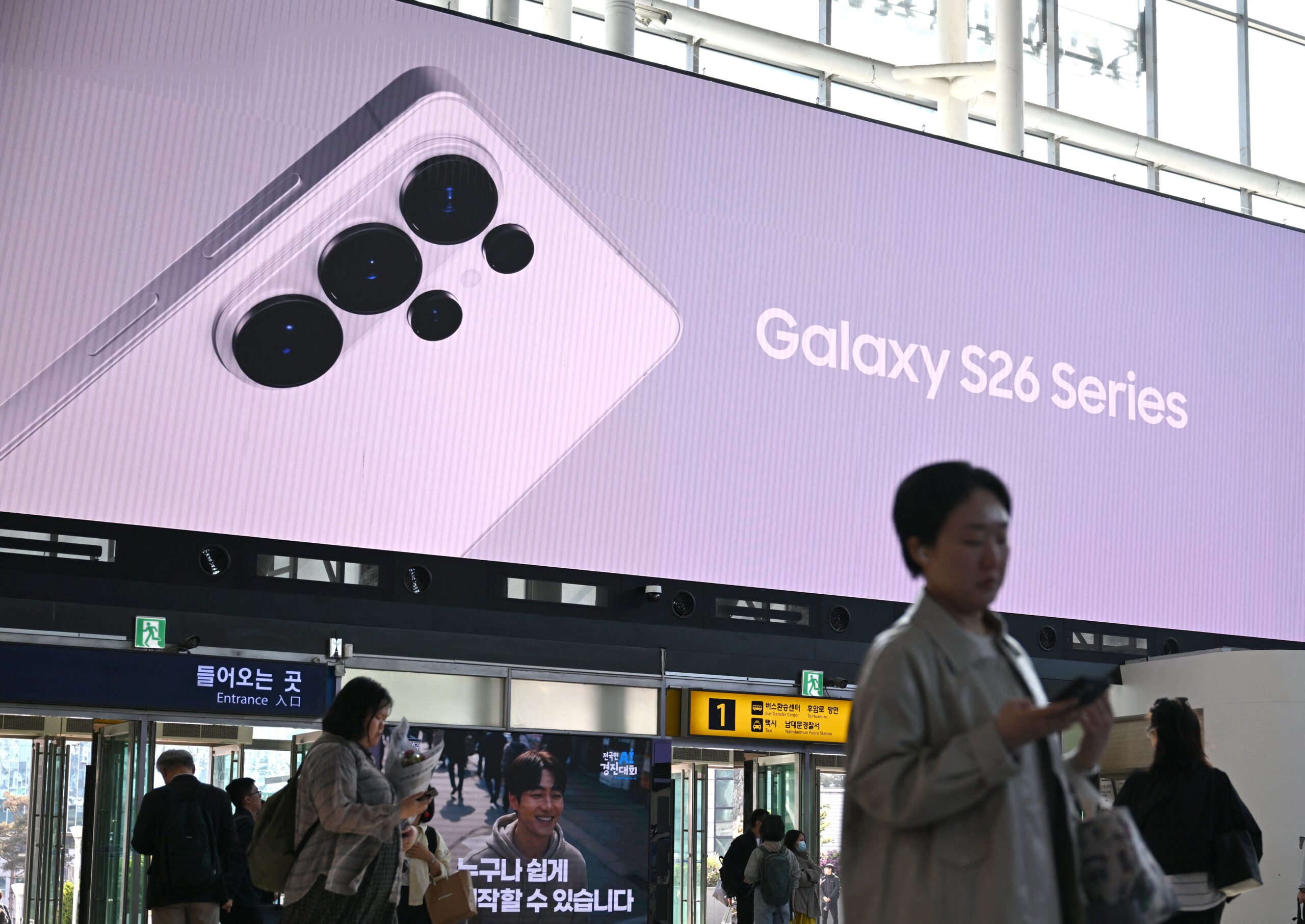 People walk past a large electronic screen advertising the Samsung Galaxy S26 smartphone