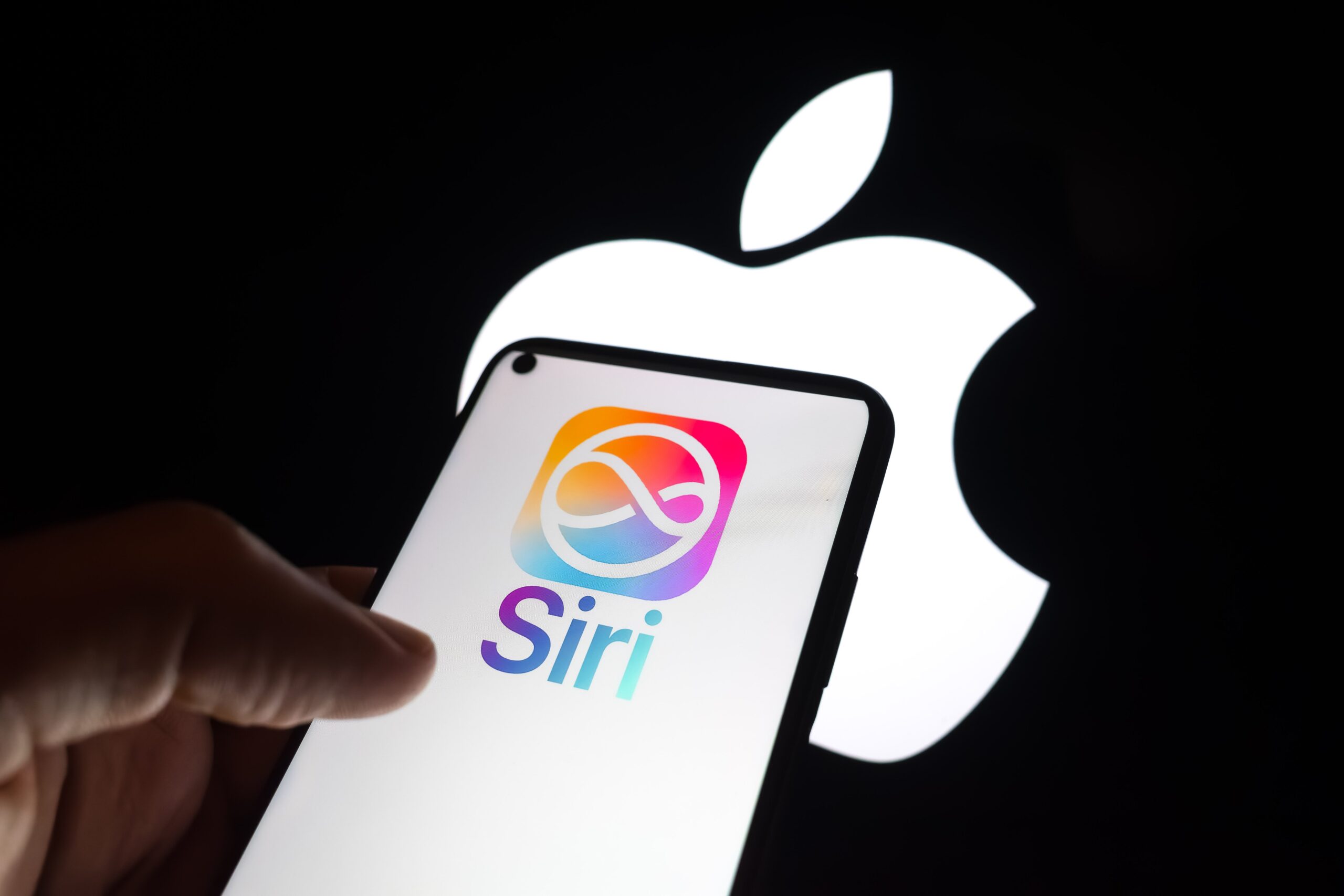 The Siri logo appears on a smartphone screen, and the Apple logo displays as the background on a laptop computer screen