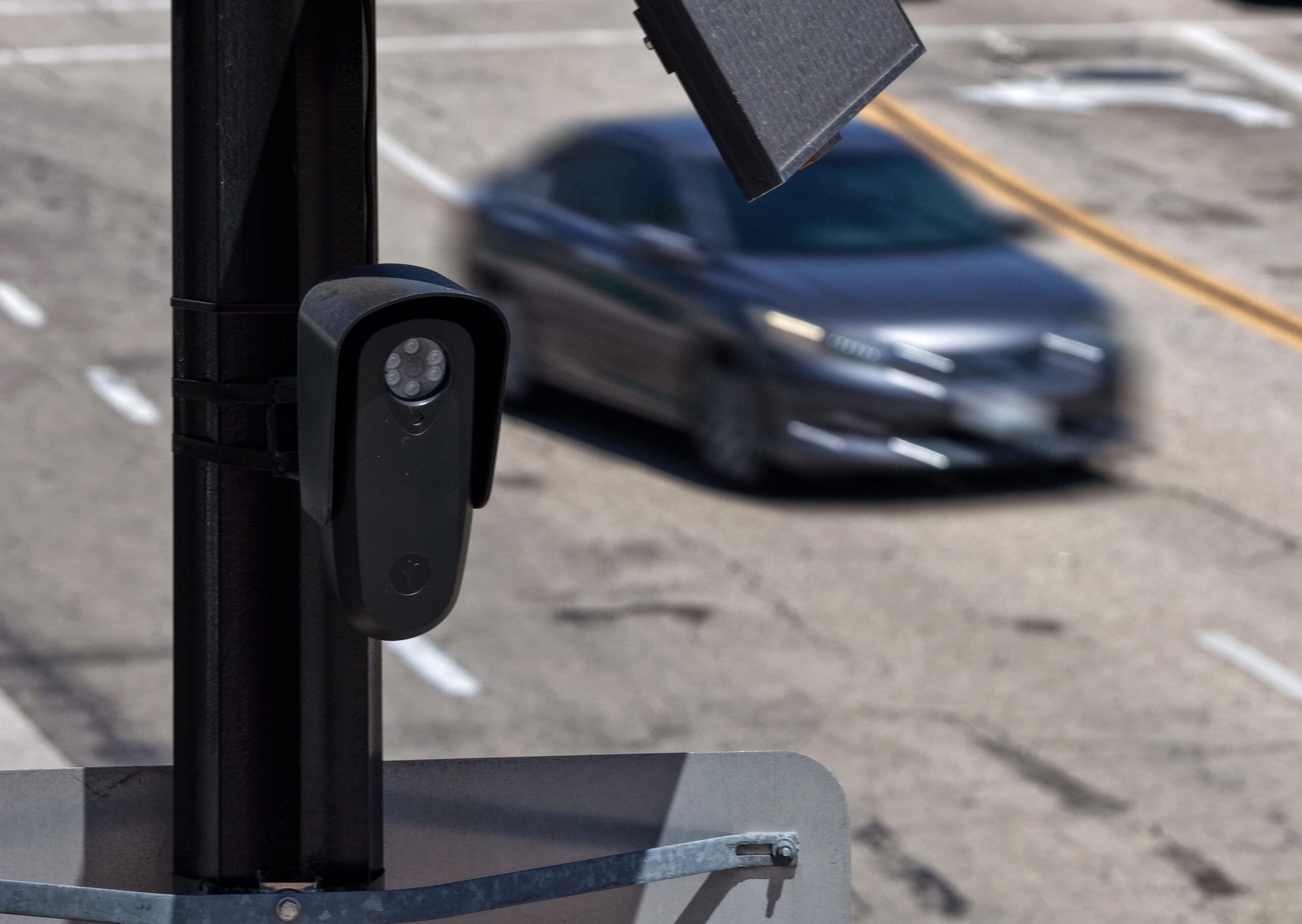 A Flock camera on a lamppost above a speeding car. 