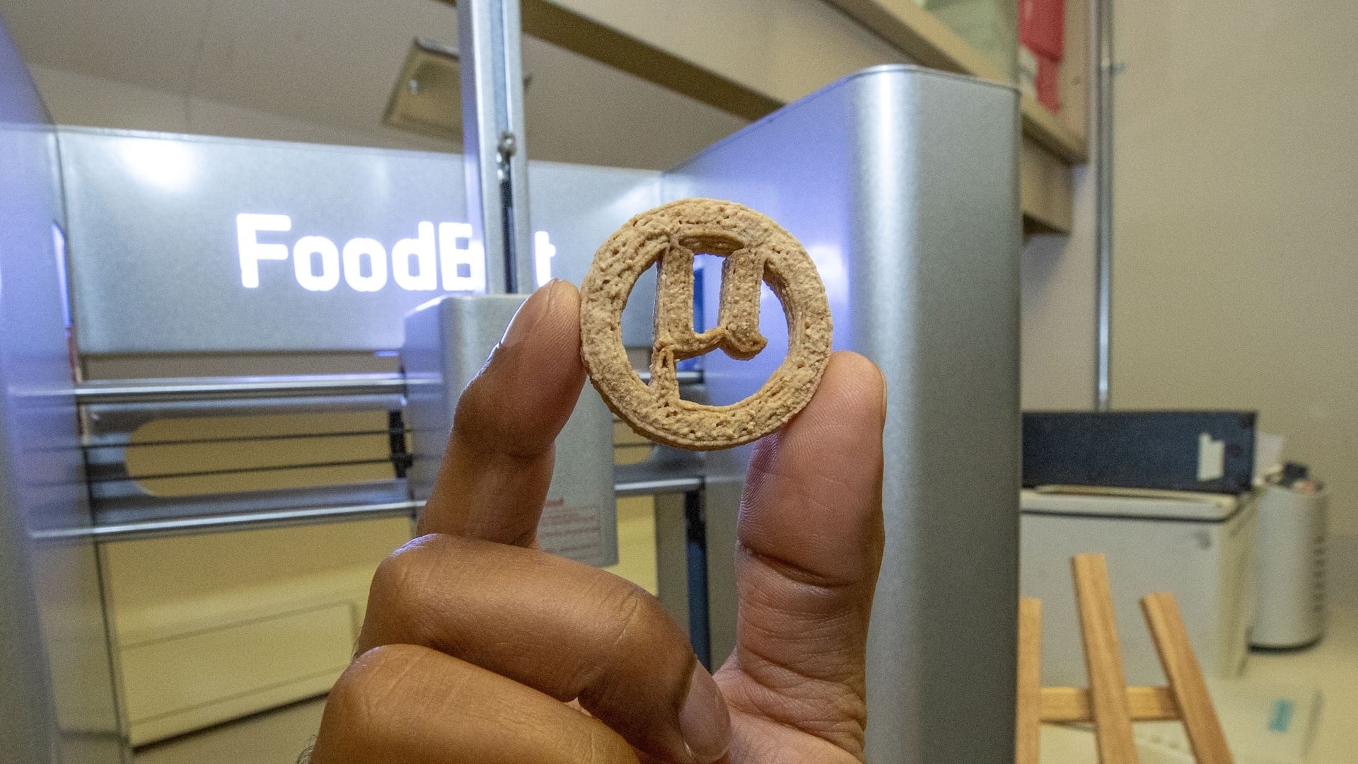 A 3D printed cookie in a person's hand in a lab.